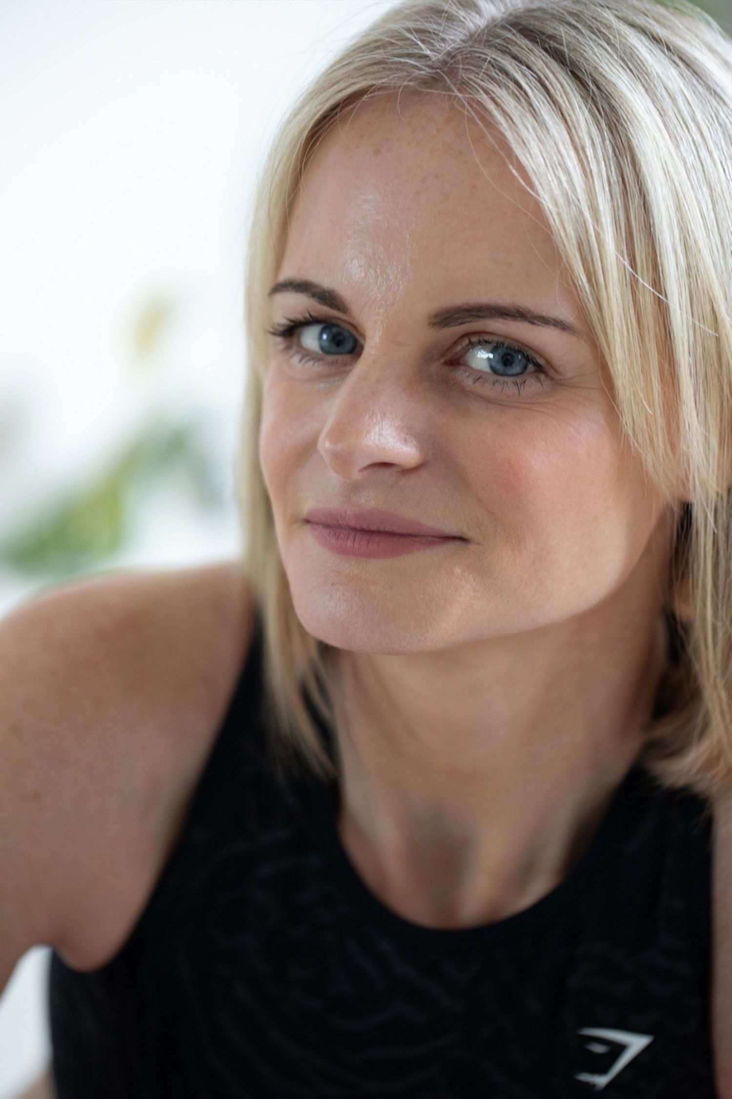 A portrait of someone with blonde hair wearing a black sleeveless top and a gentle smile.