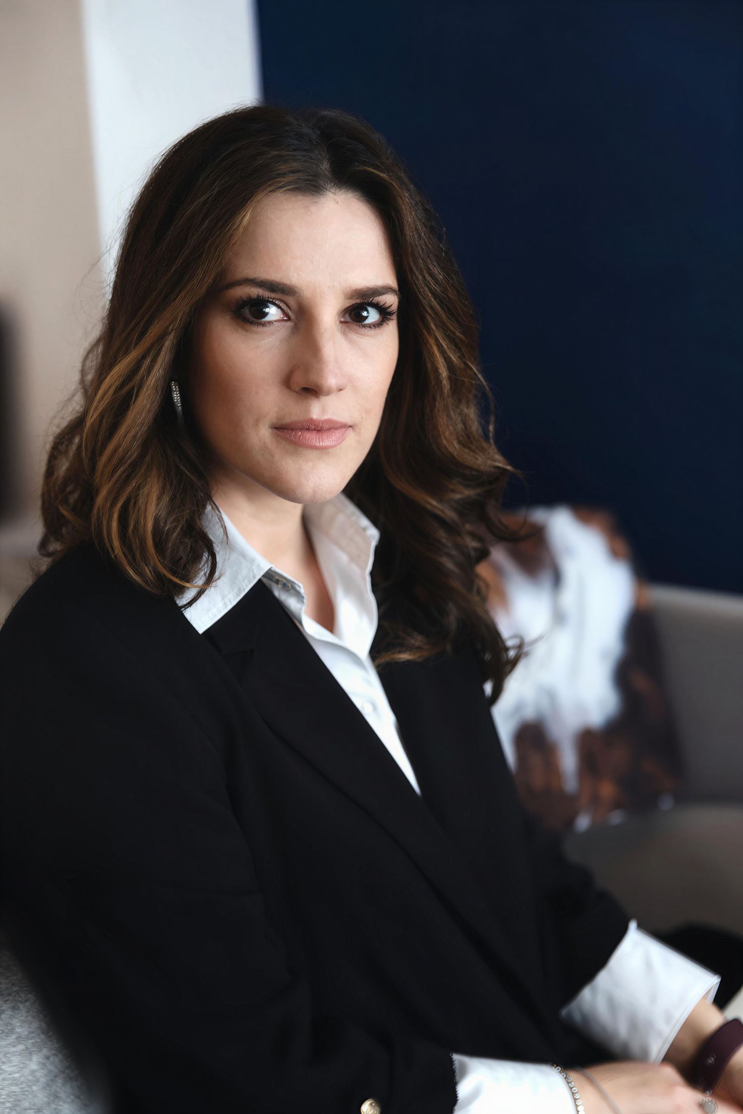 Professional wearing a black blazer and white collared shirt sits in a casual pose.