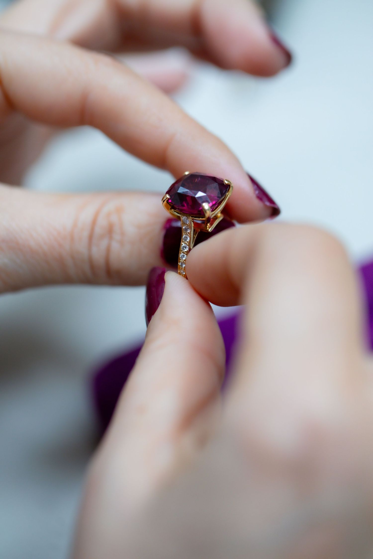 Close up macro shot of hands examining a purple gemstone ring with diamond accents in natural lighting.