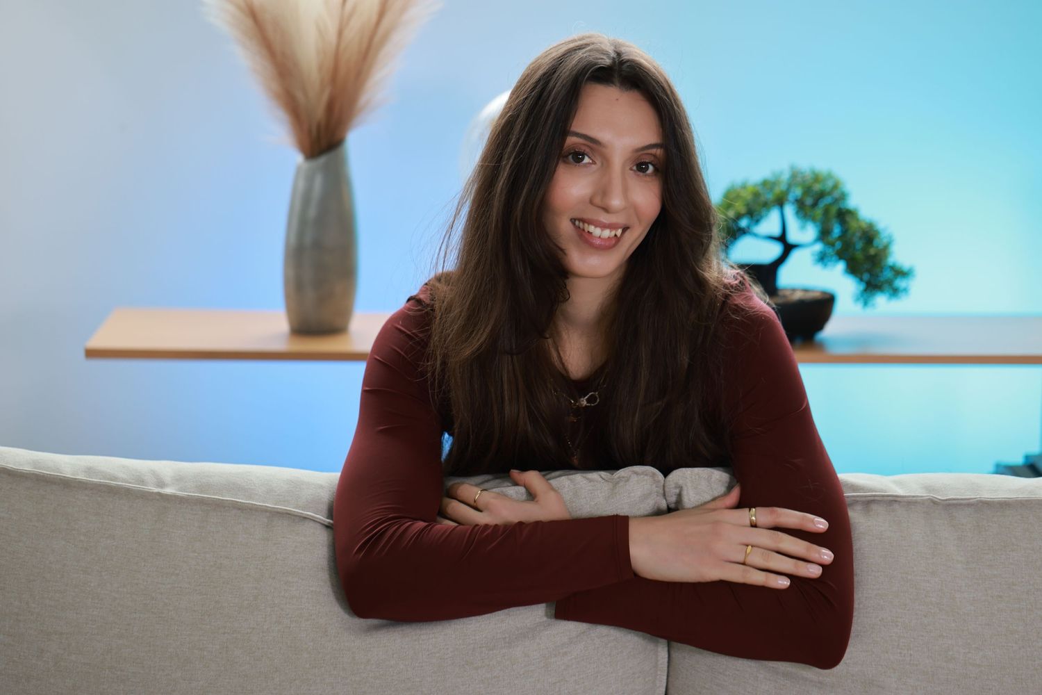 A person in a burgundy sweater leans on their elbows while sitting at a desk against a bright blue background.