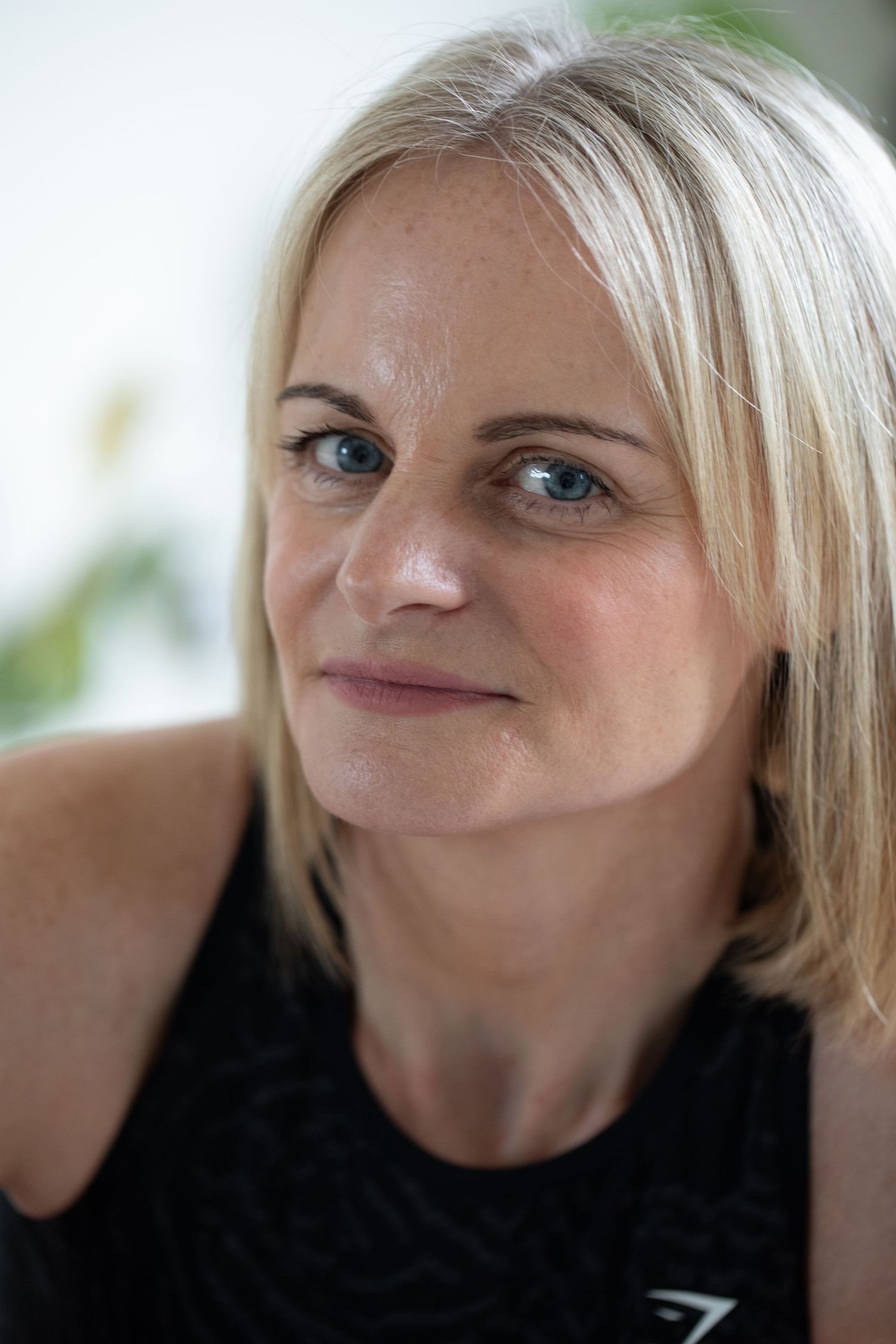 Close up portrait of someone with blonde hair wearing a black sleeveless top smiling warmly at the camera.