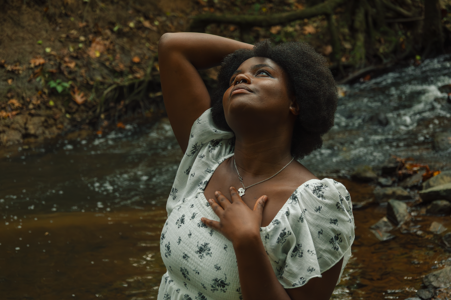 Person in floral dress striking expressive poses by a forest stream.