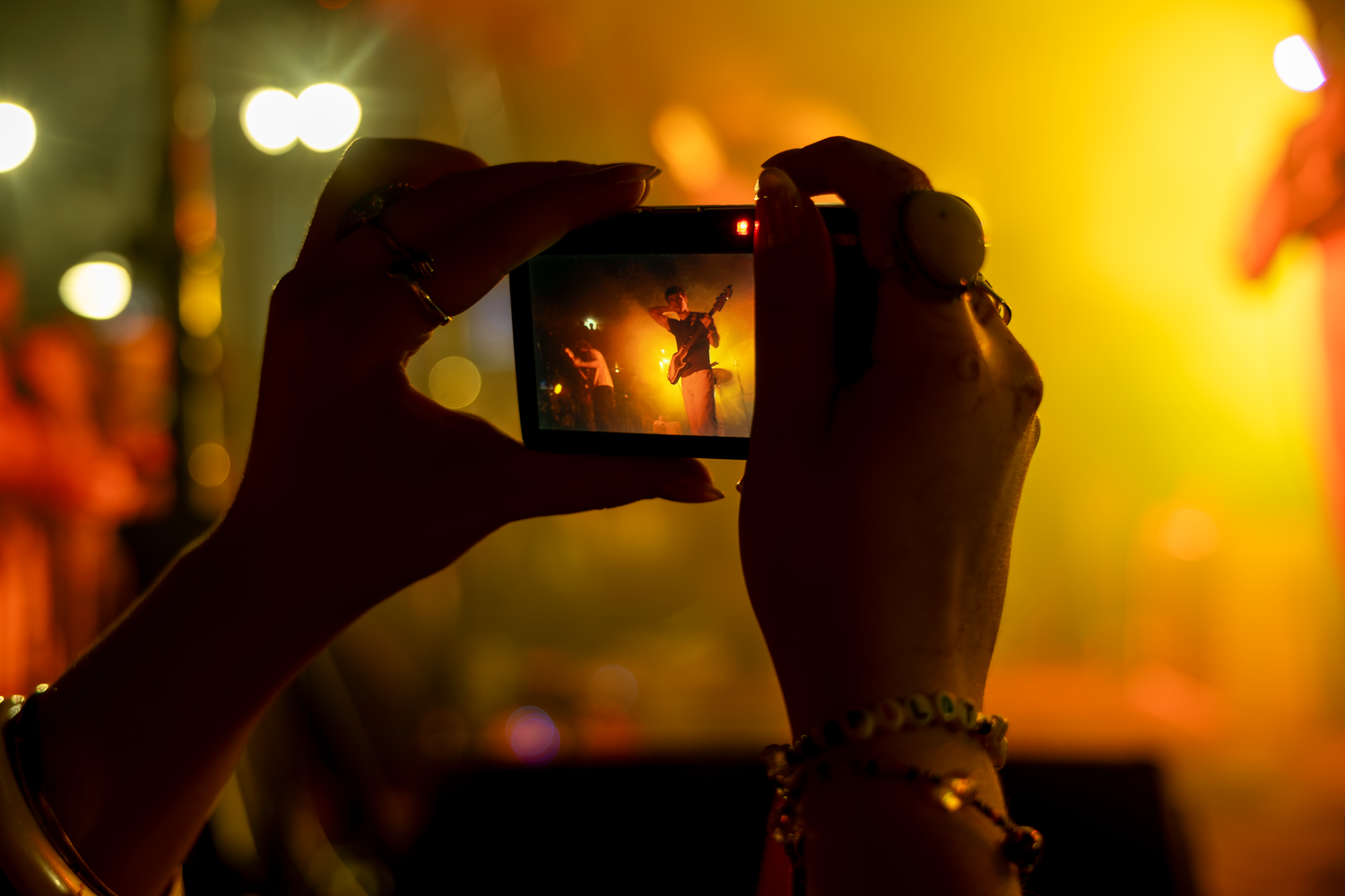 Person holding smartphone capturing a performer on stage at a concert with warm golden lights in the background.
