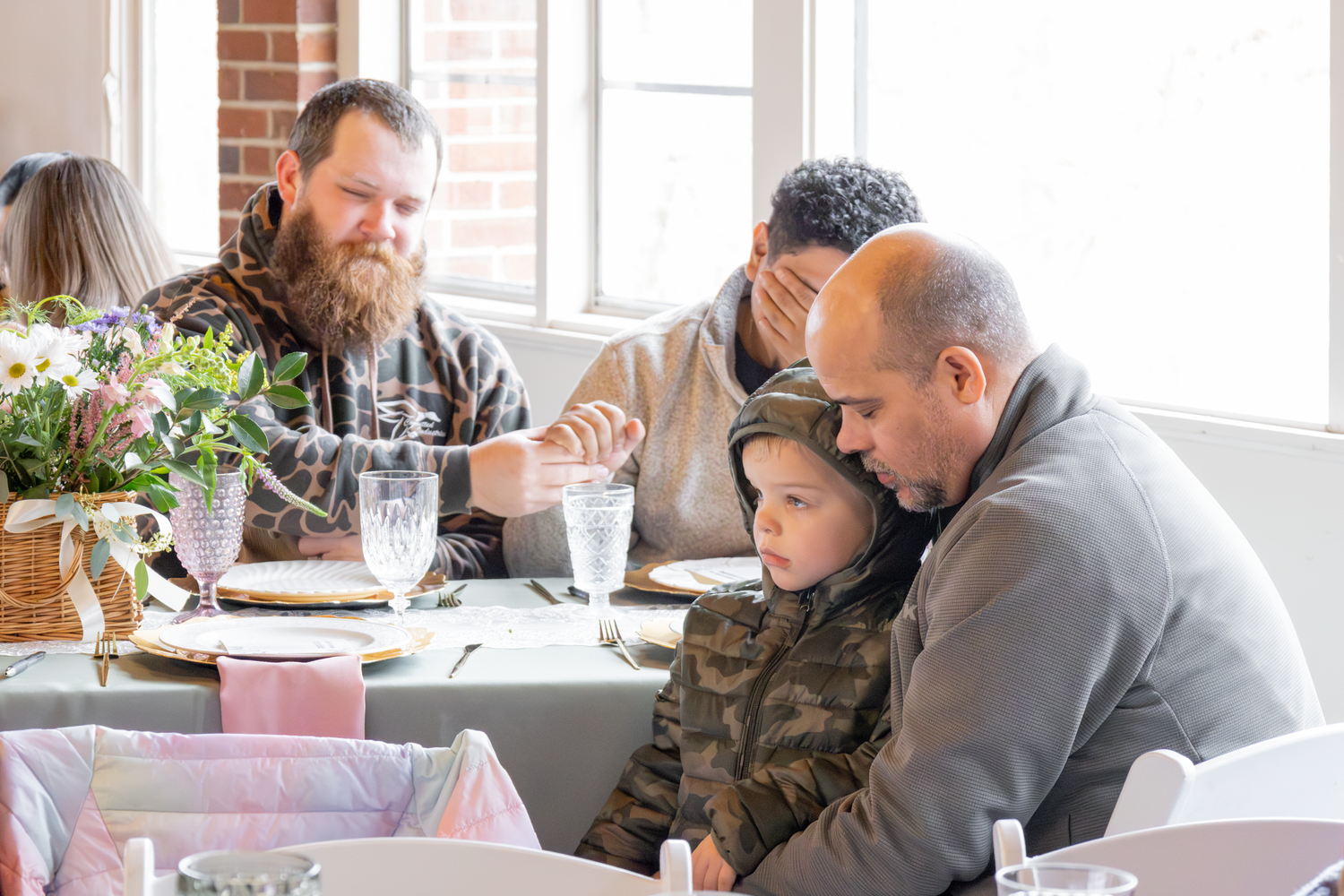 Family members gather around a table during a celebration in a rustic brick-walled venue.