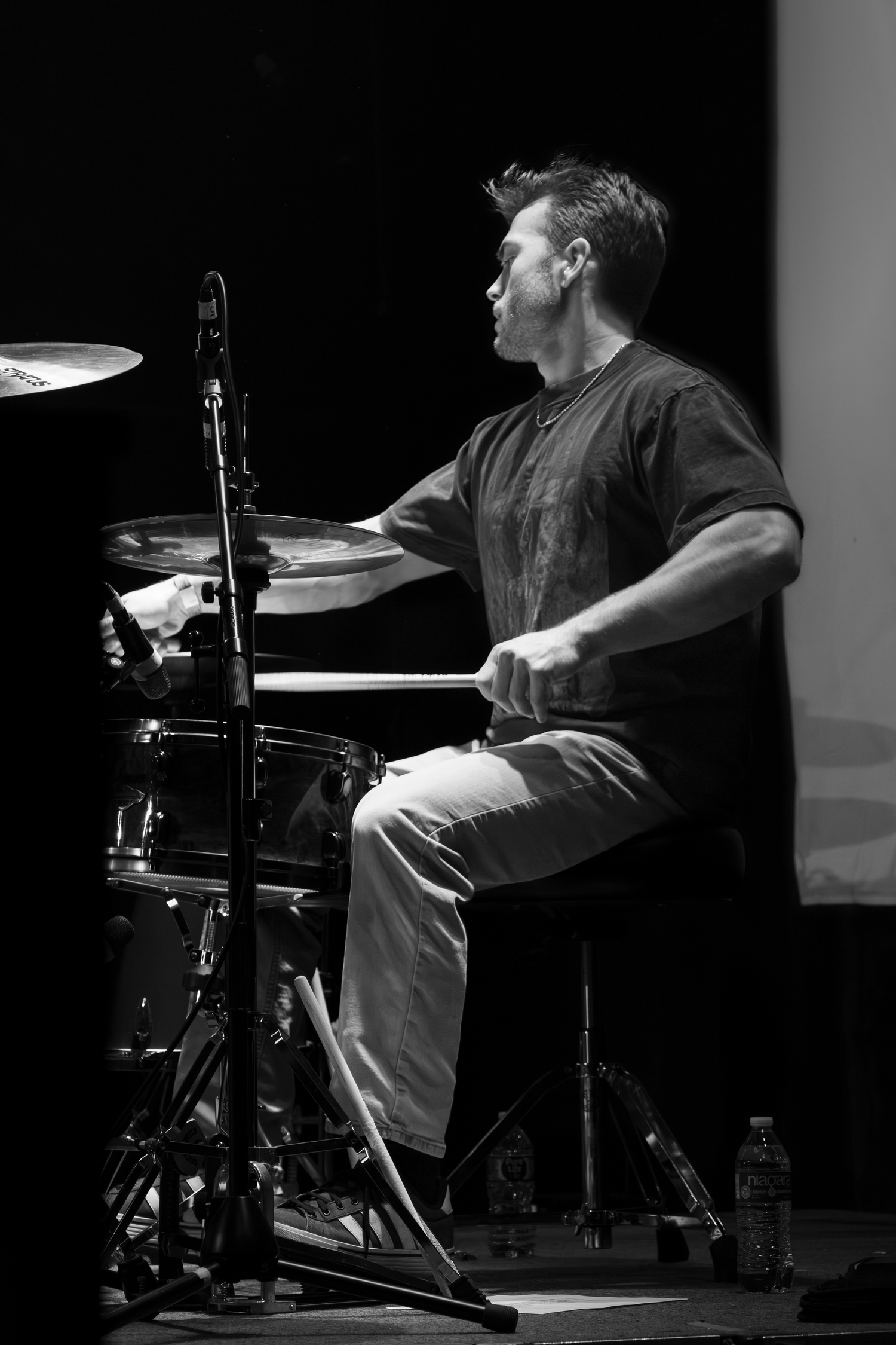 Drummer for High June performs in black and white on a drum kit during a concert.