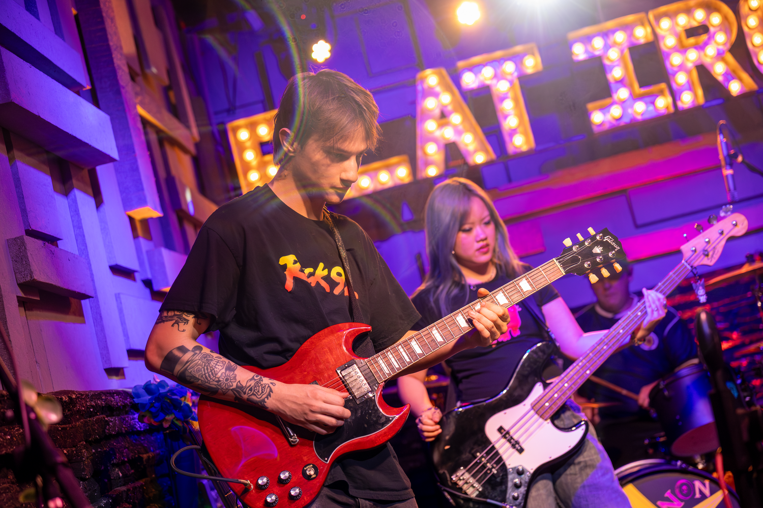 Two guitarists performing on stage under colorful lights at a live rock music venue.