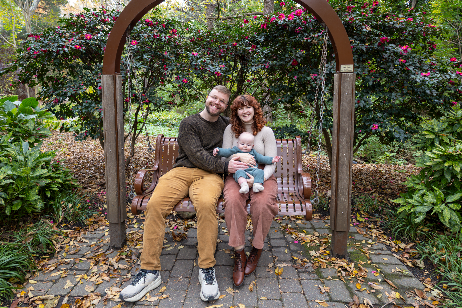 A couple embraces on a rustic garden bench surrounded by blooming flowers and greenery at Tanger Family Bicentennial Garden.