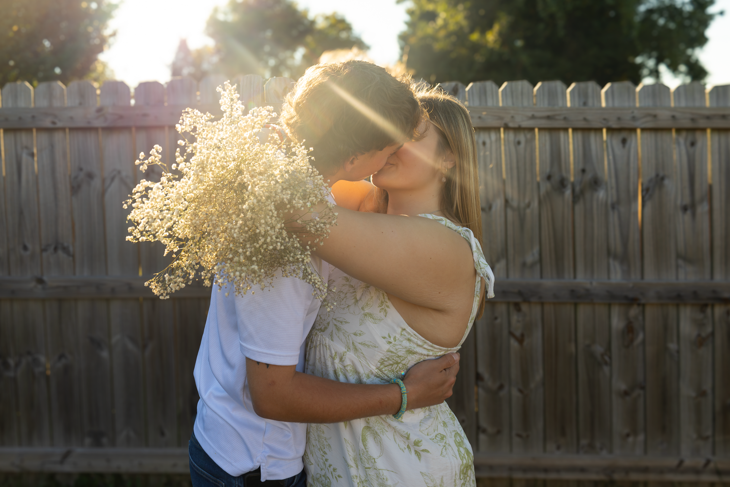 Romantic sunset embrace with delicate baby's breath flowers against wooden fence background.