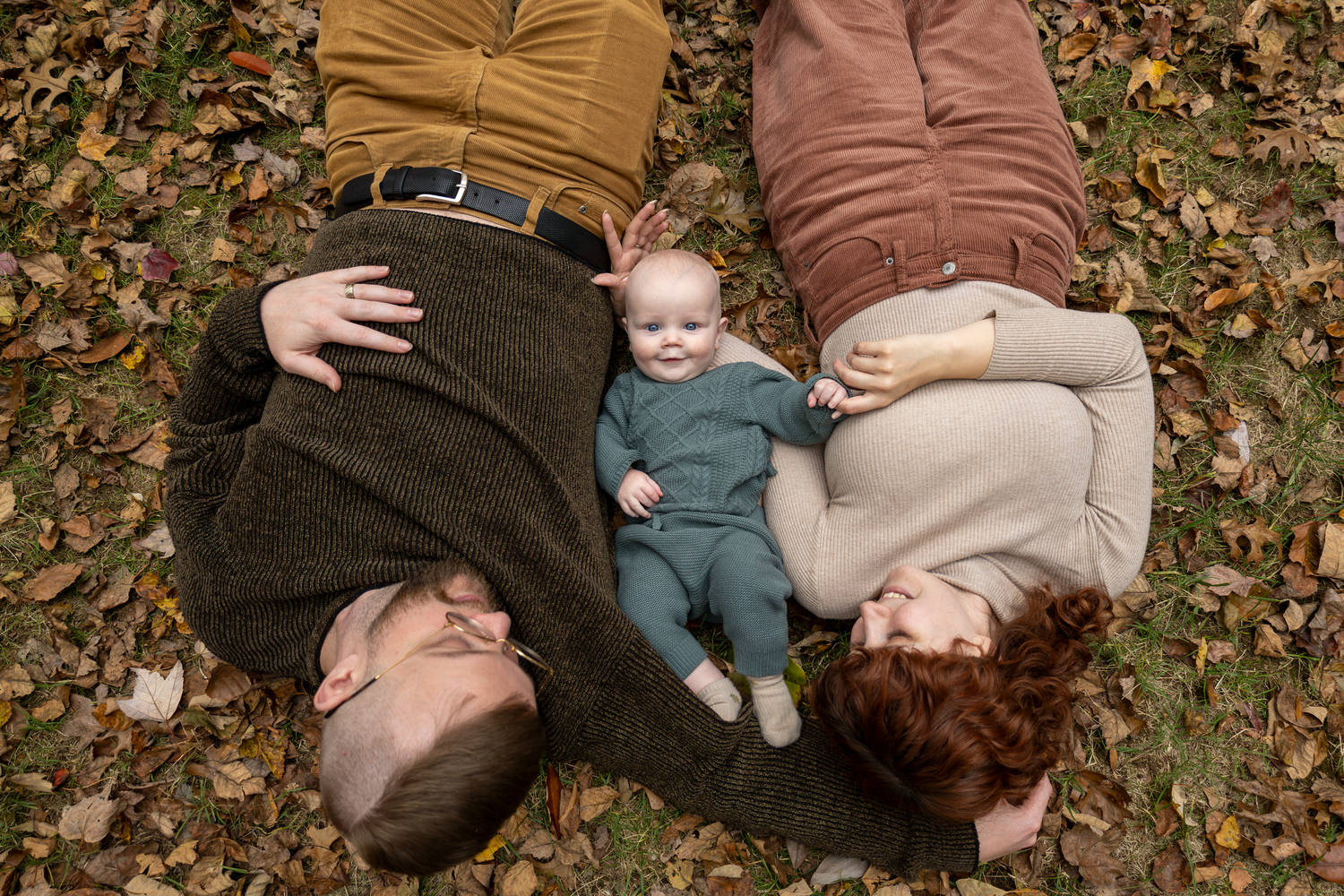 A family lying together on fallen autumn leaves in a park at Tanger Family Bicentennial Garden.