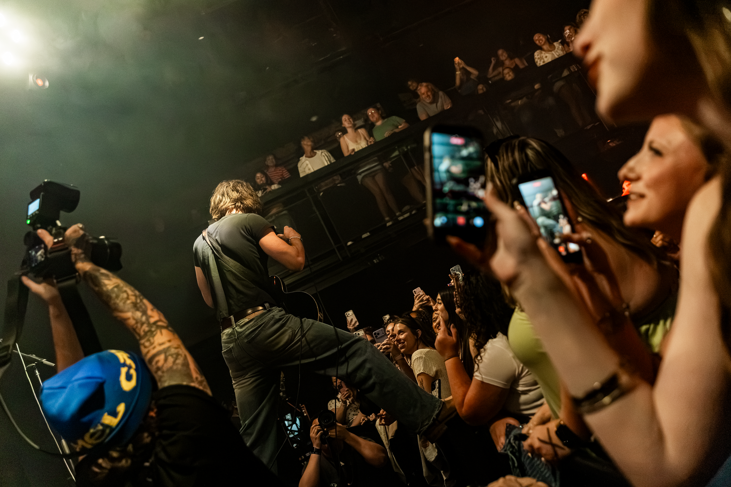 Performer crowd surfing at a live concert while fans cheer and record with phones in a dark venue.