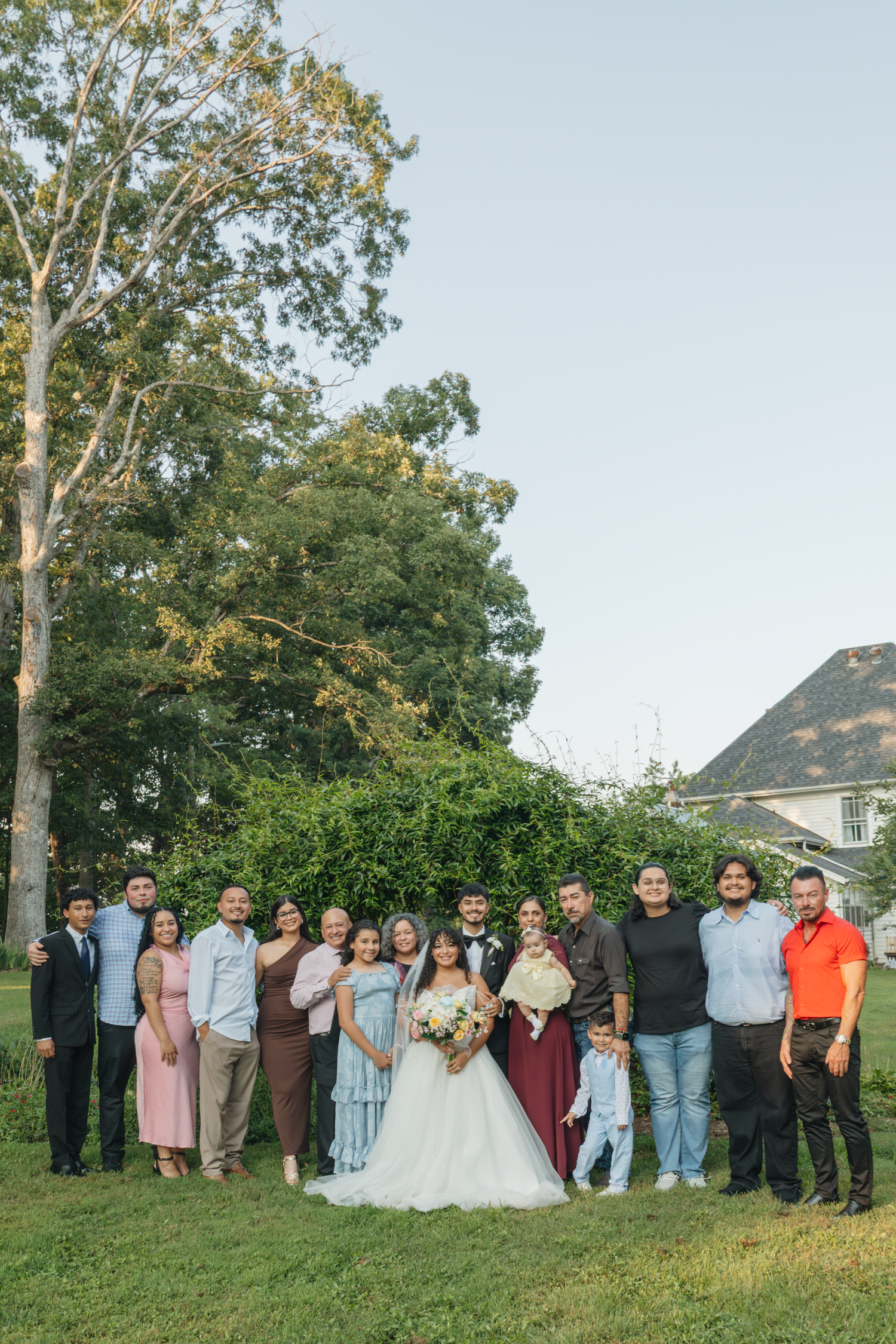 Large group wedding photo with guests lined up outdoors against trees and blue sky at The Farmhouse Siloam.