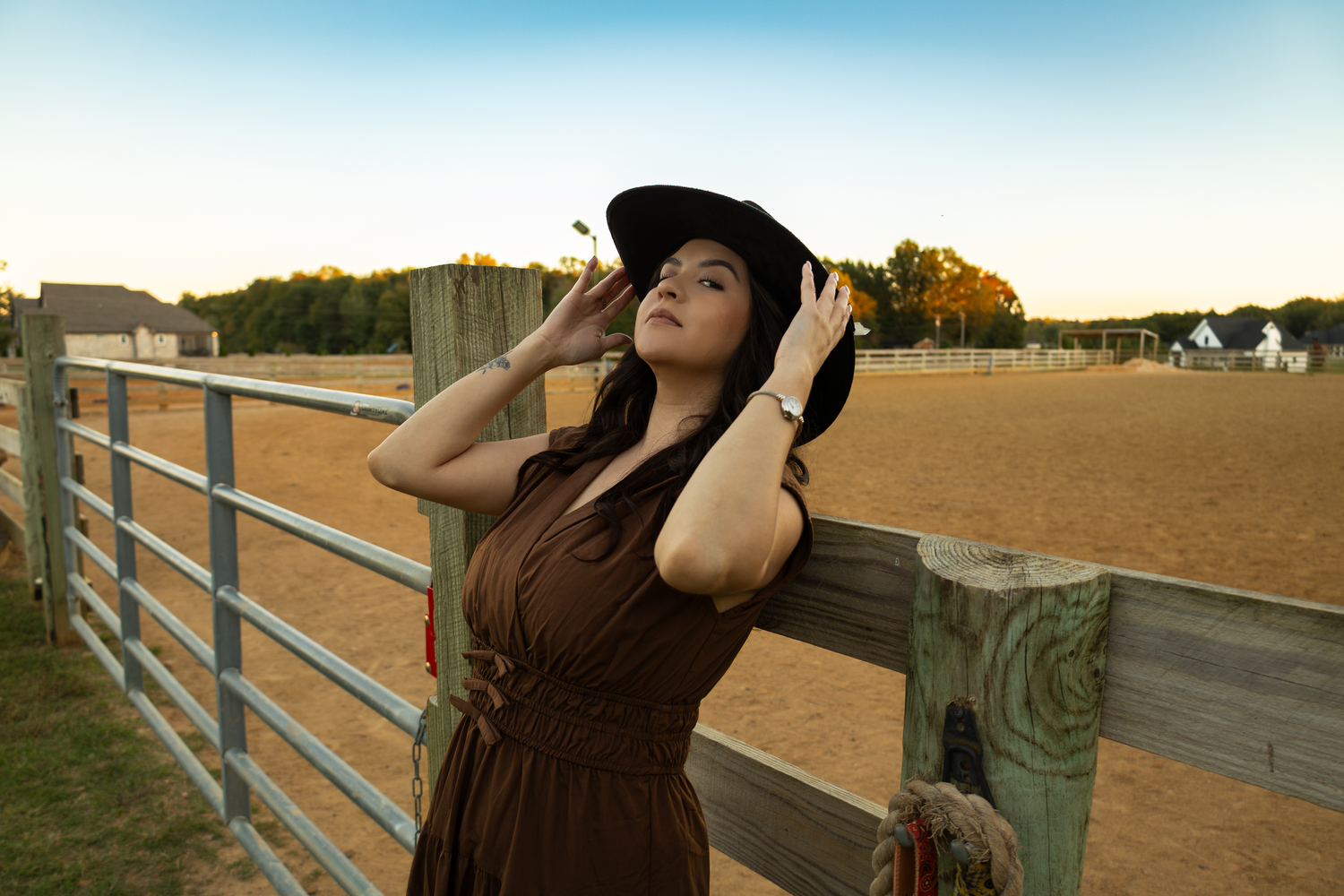 Person in dress and hat enjoying sunset by fence in rural setting.