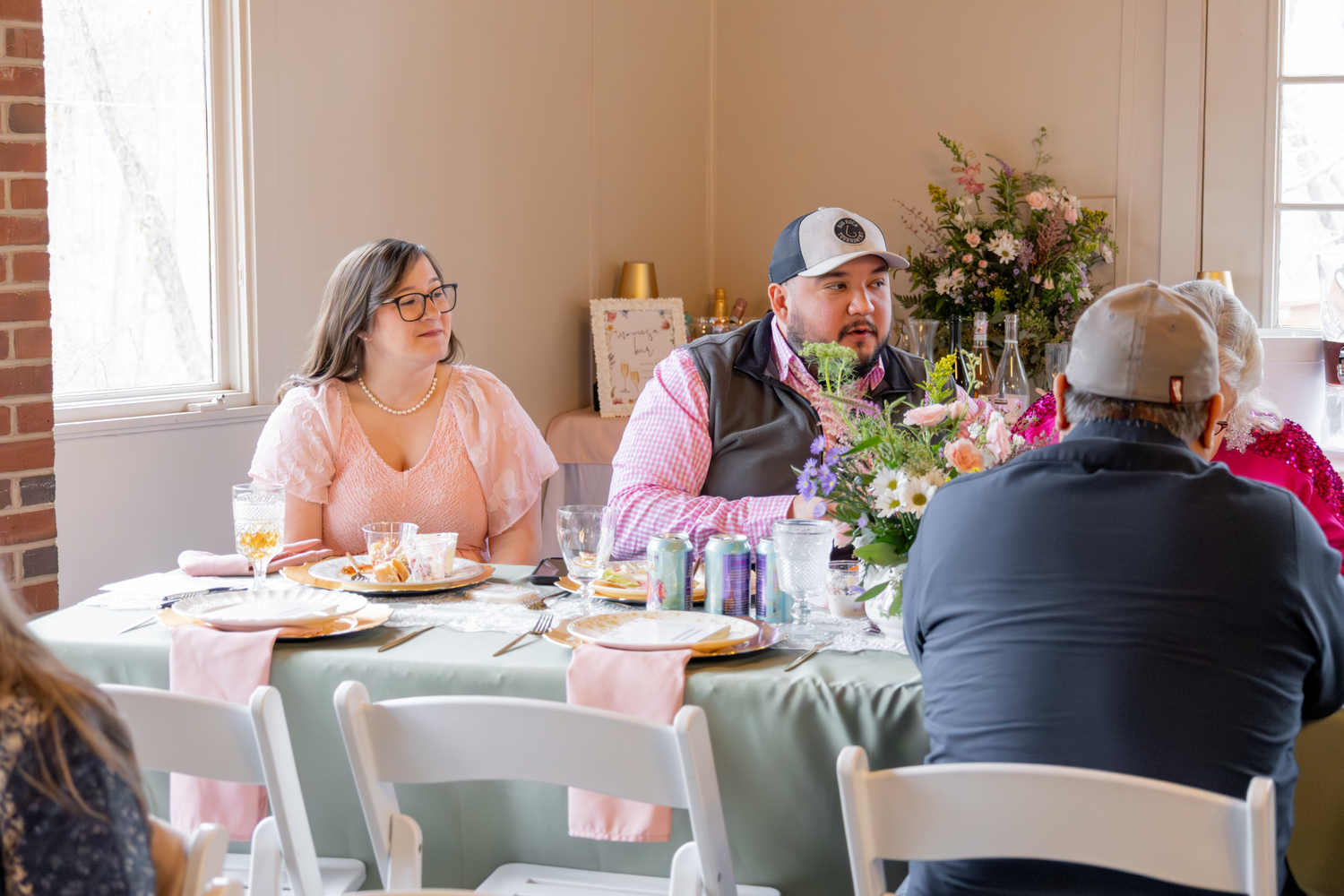 Guests seated at tables with mint green tablecloths enjoy a casual indoor gathering with floral centerpieces.