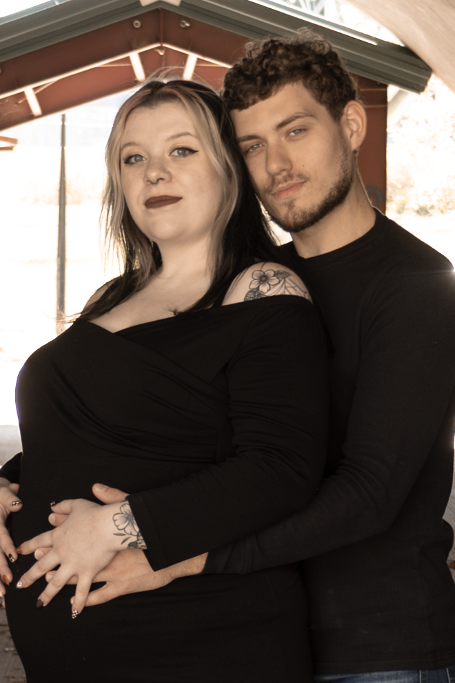Couple in black clothing posing together in romantic maternity photo shoot at Lydia's Bridge.