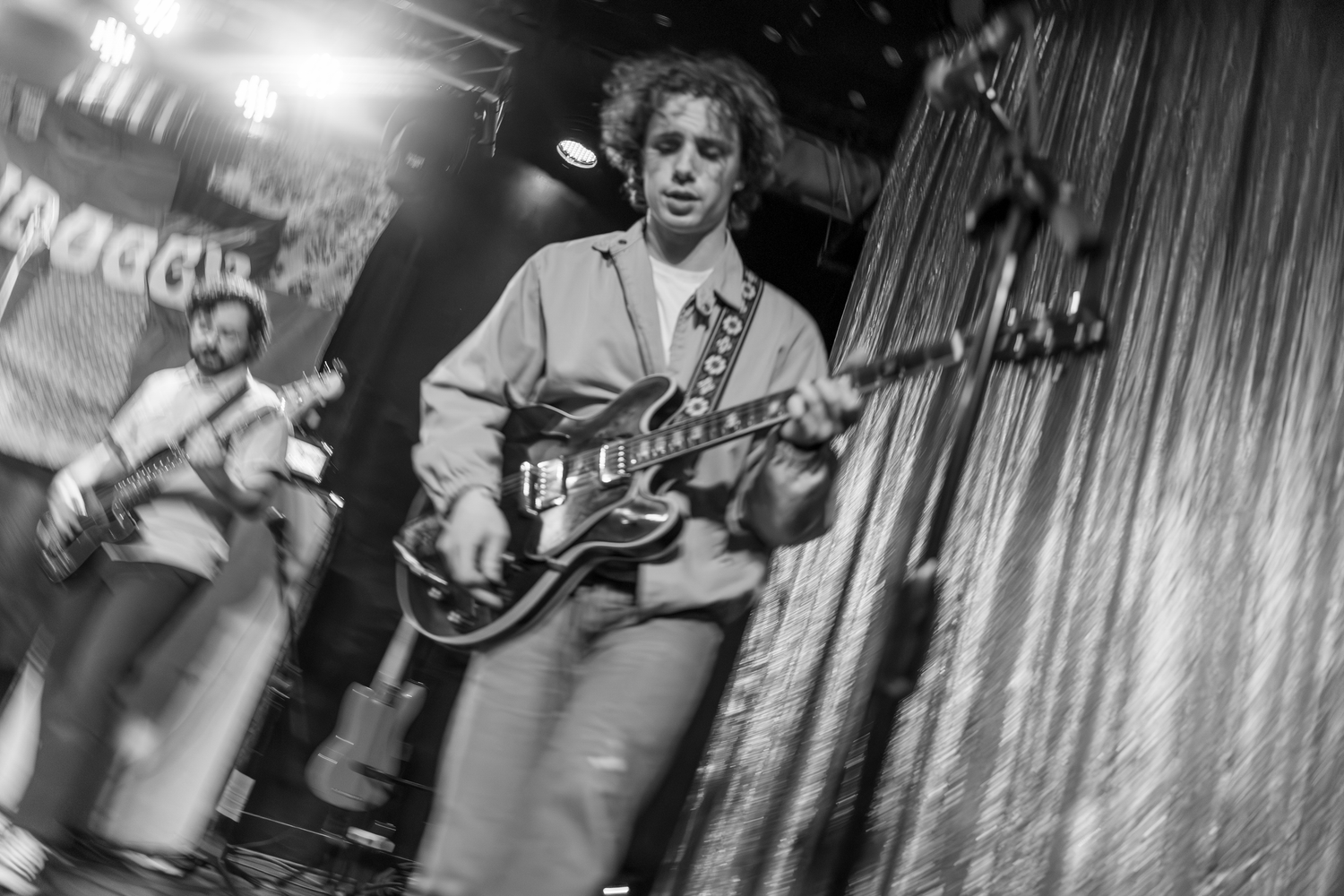 A musician performs on stage with an electric guitar in a black and white concert photograph.