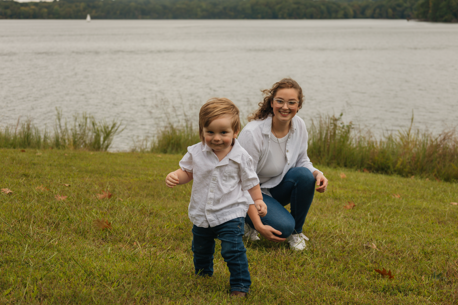 Family playing and running together on grassy hill near water.