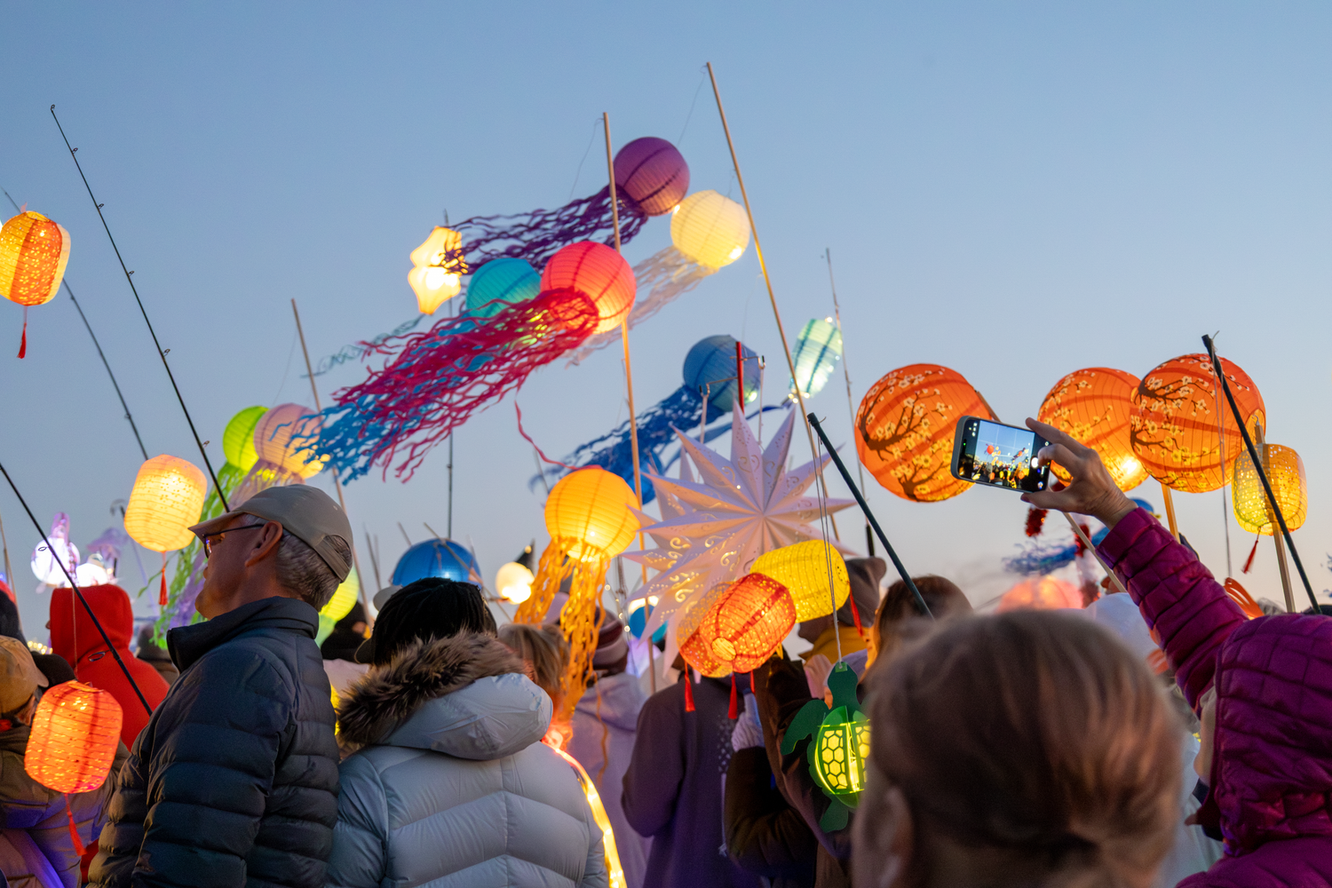 Colorful illuminated lanterns and kites fill the twilight sky at a festival in Oak Island.