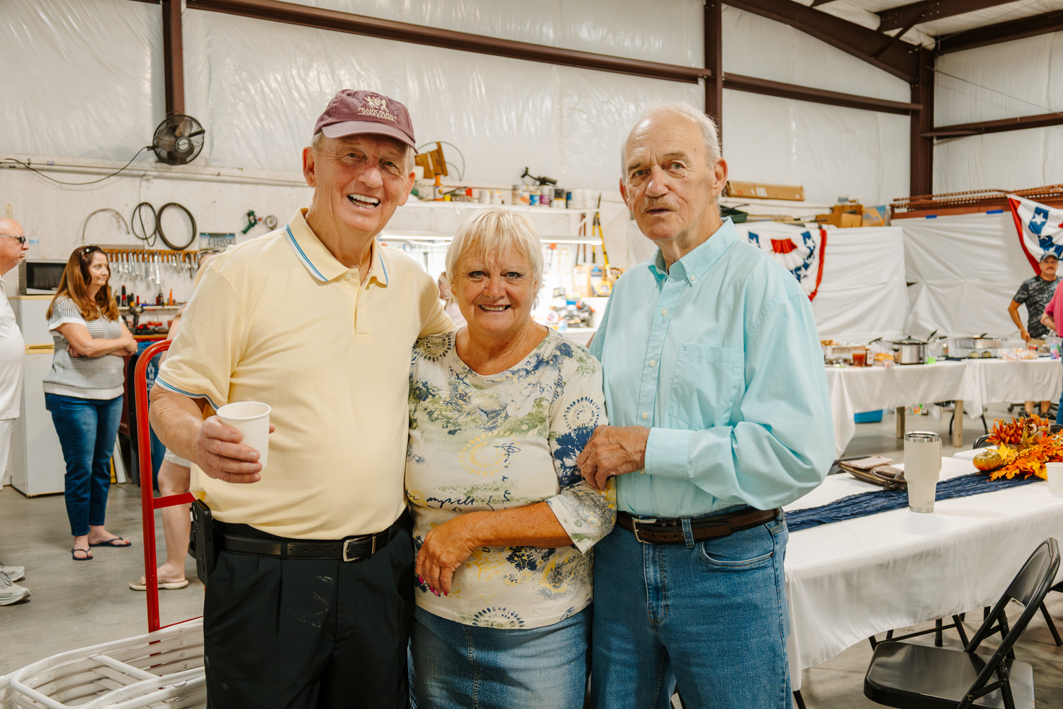 Three people pose together at a casual indoor event with decorations visible in the background.