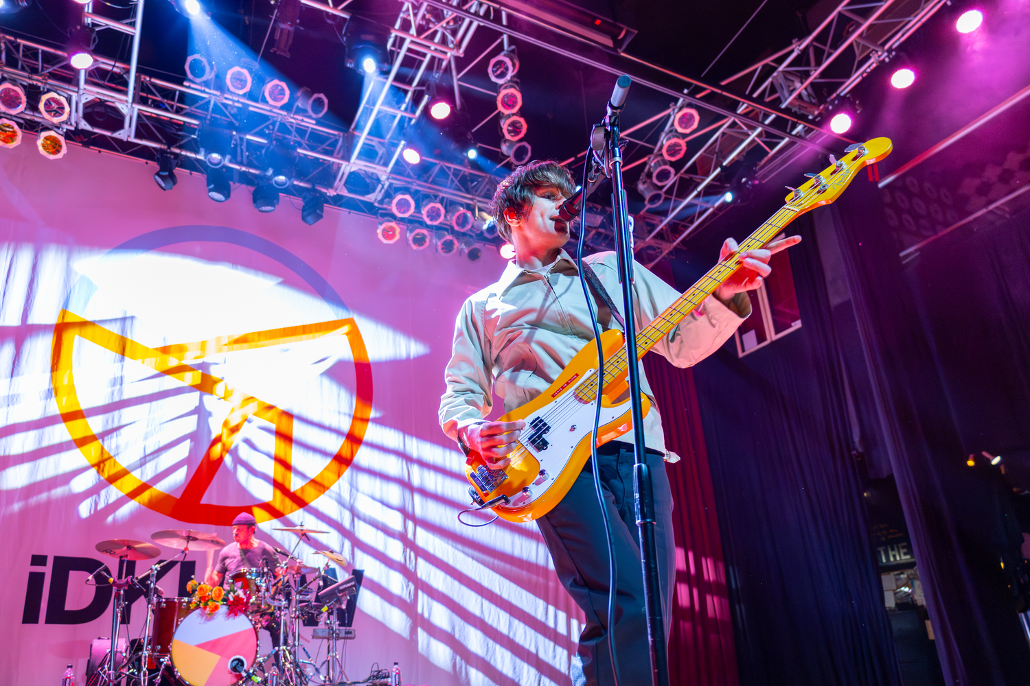 Dallon Weekes on concert stage with vibrant purple and blue lighting effects and technical equipment setup.