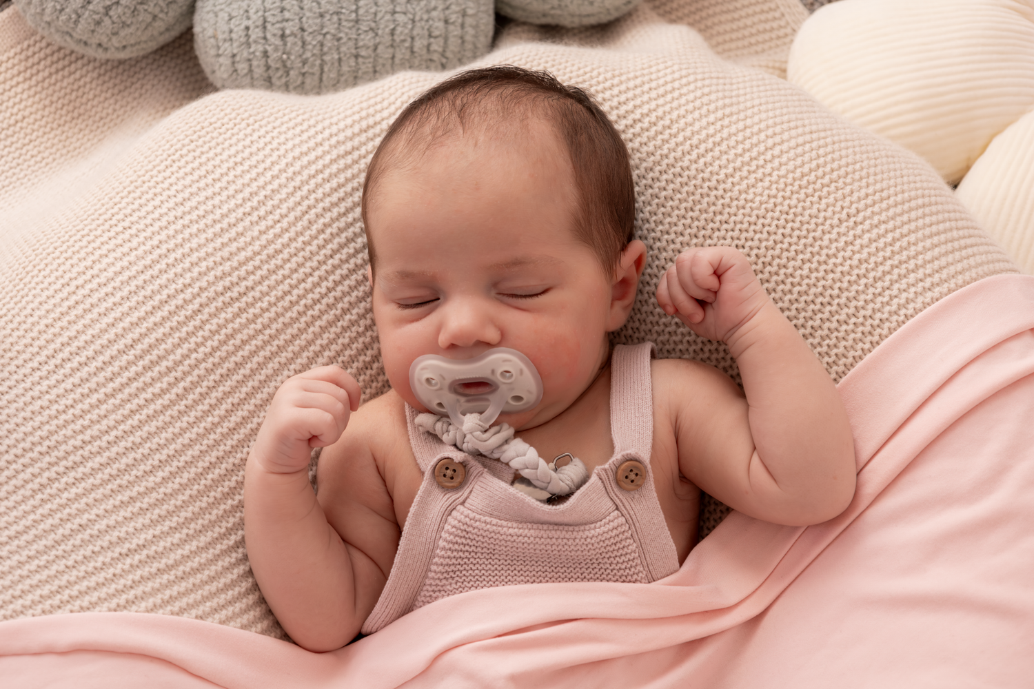 Sleeping newborn baby lying on soft pink bedding wearing knit accessories.