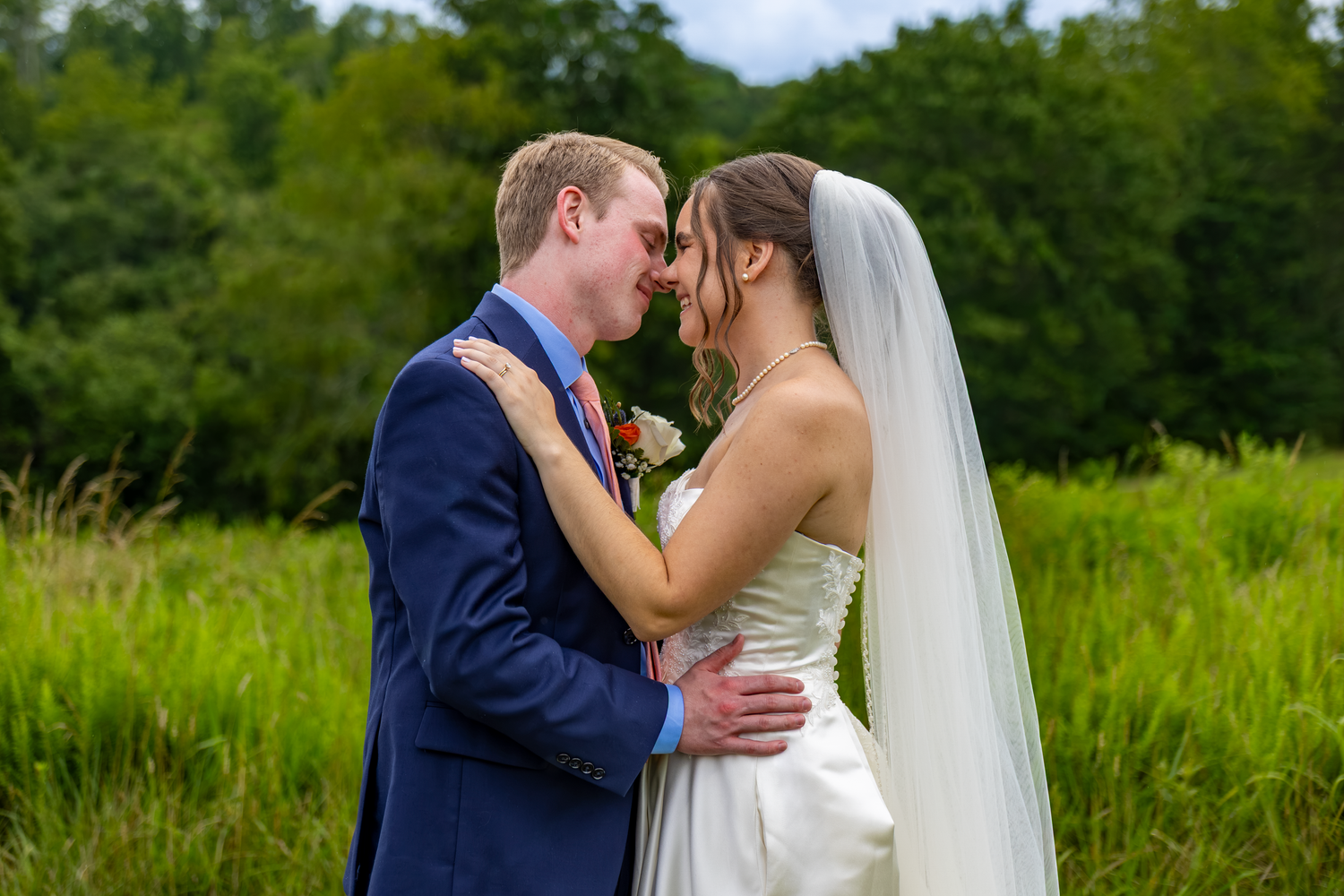 A bride and groom share a romantic moment outdoors, surrounded by lush green fields on their wedding day.