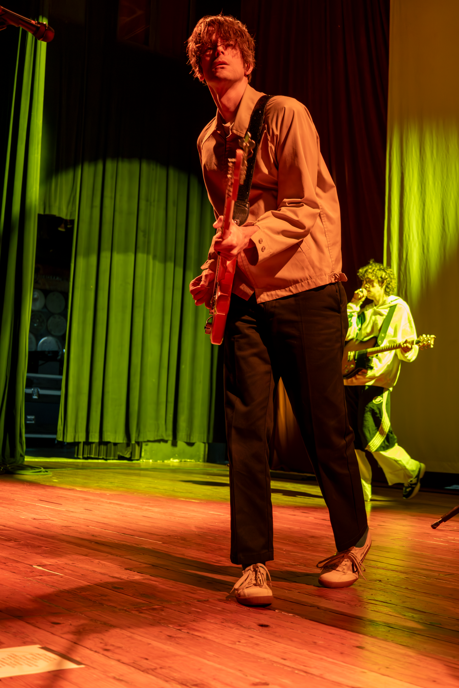 Dallon Weekes performing on stage bathed in warm orange and green theatrical lighting.