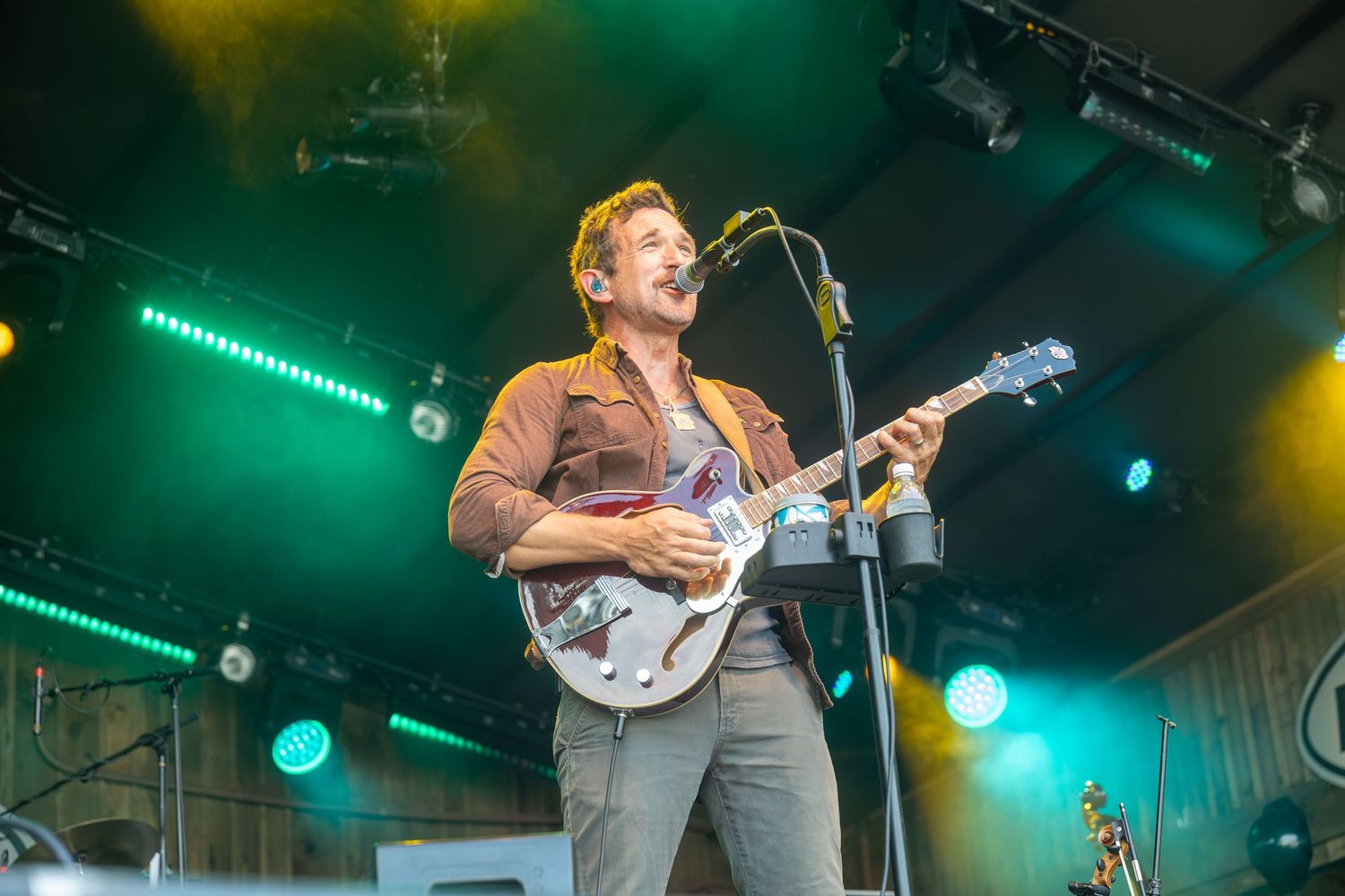 Male guitarist performs on stage with green and teal stage lighting during an outdoor concert.