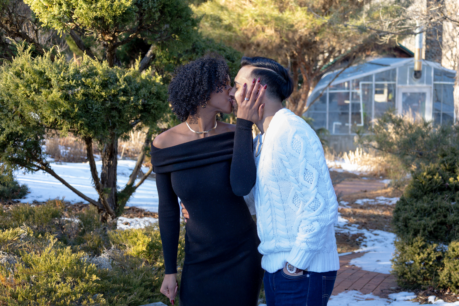 A couple embraces tenderly in front of a house on a sunny winter day.