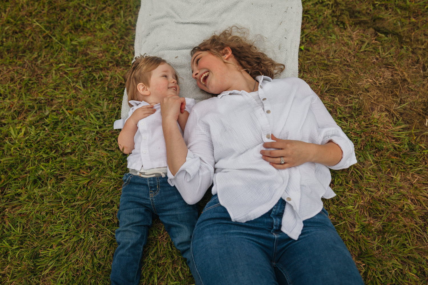 Family members relaxing together on blanket in grassy outdoor setting.
