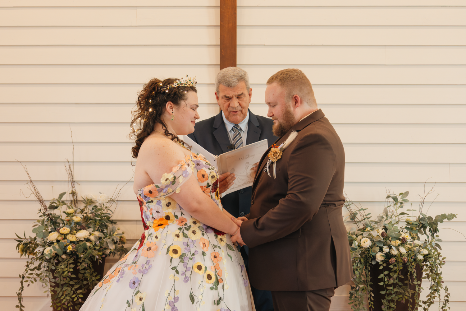 Romantic outdoor wedding ceremony moments captured in front of white chapel wall.