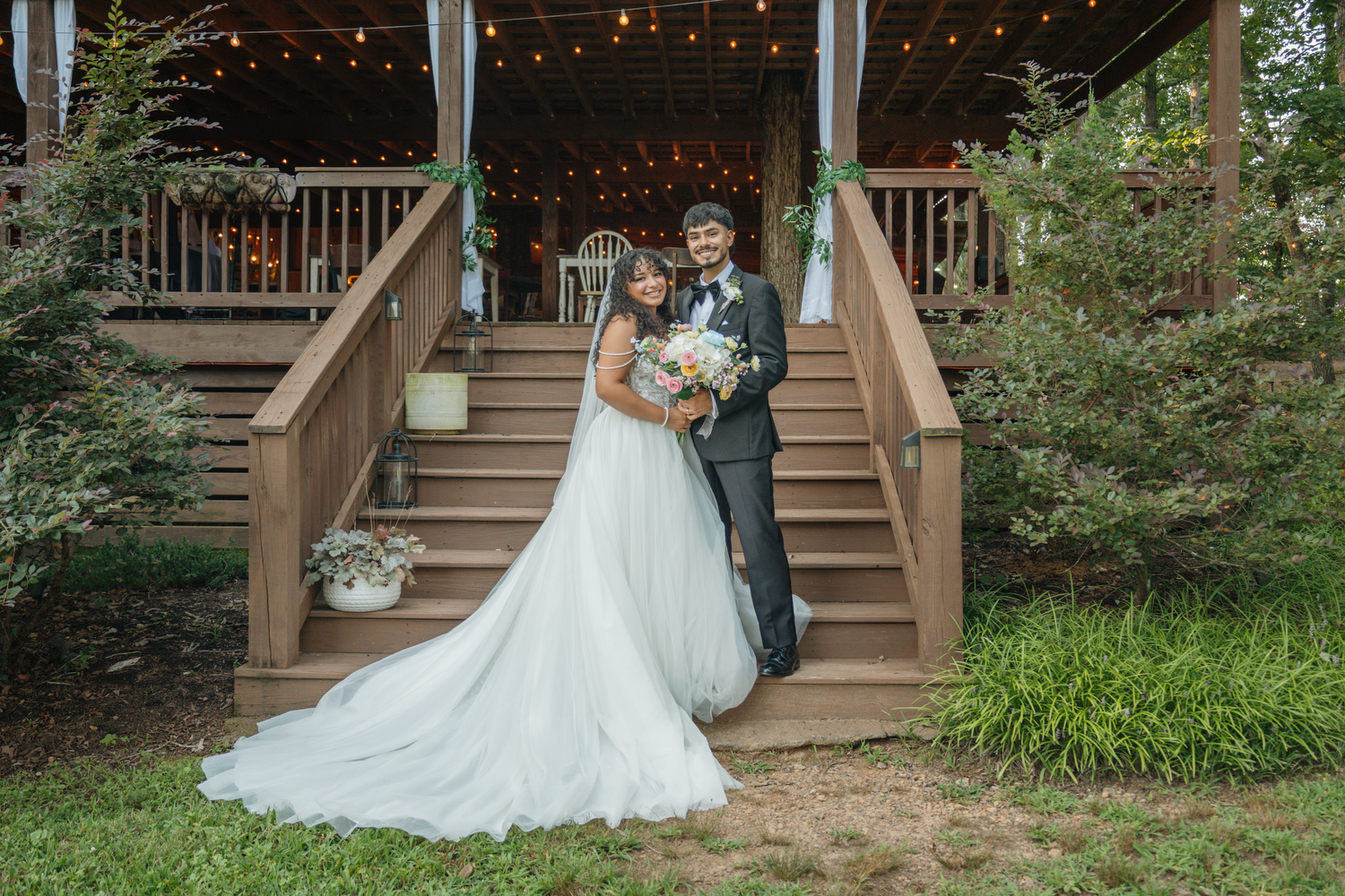 Wedding photos on wooden steps decorated with string lights and natural landscaping at The Farmhouse Siloam.