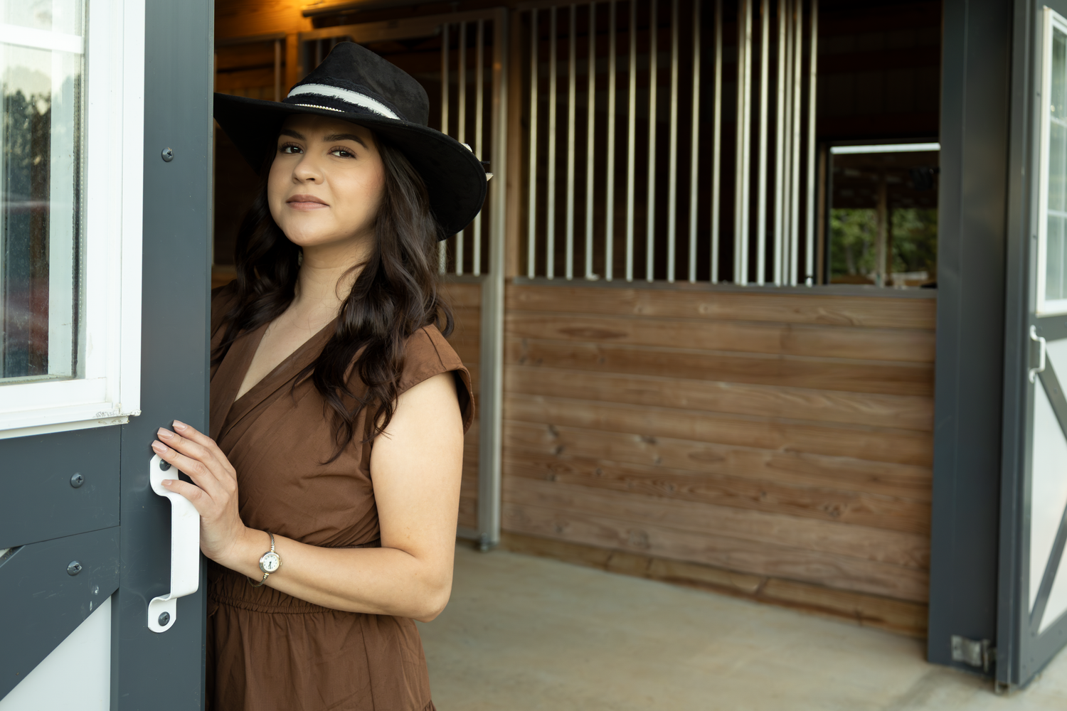 Person wearing brown dress and hat standing in rustic barn doorway.