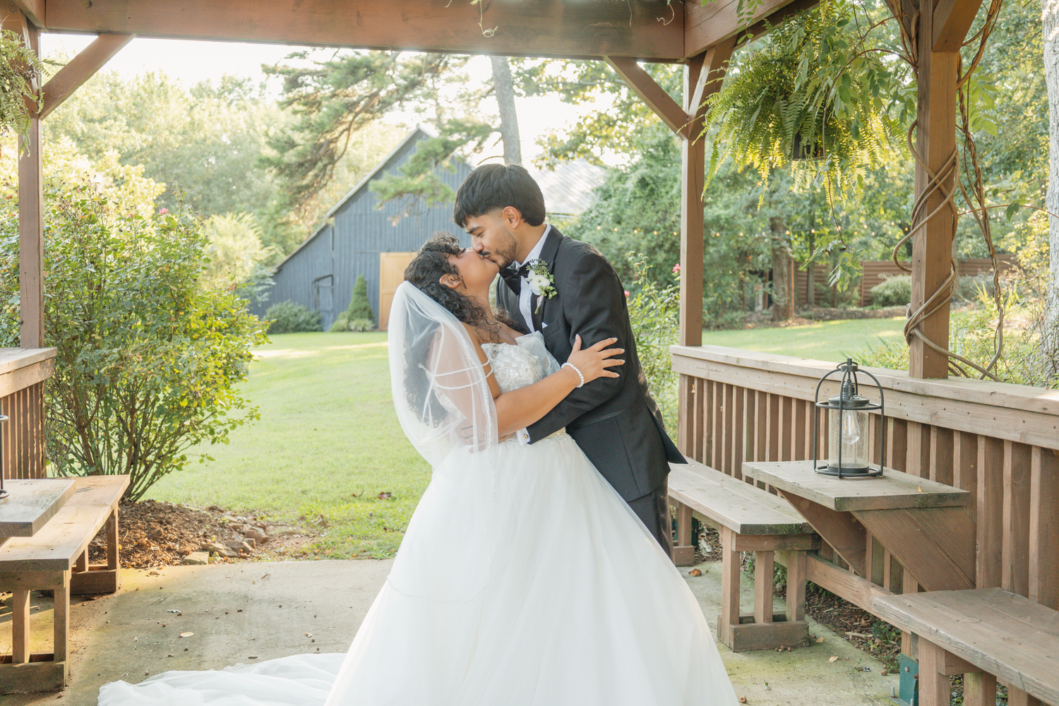 A romantic wedding moment captured under a wooden gazebo surrounded by lush greenery at The Farmhouse Siloam.