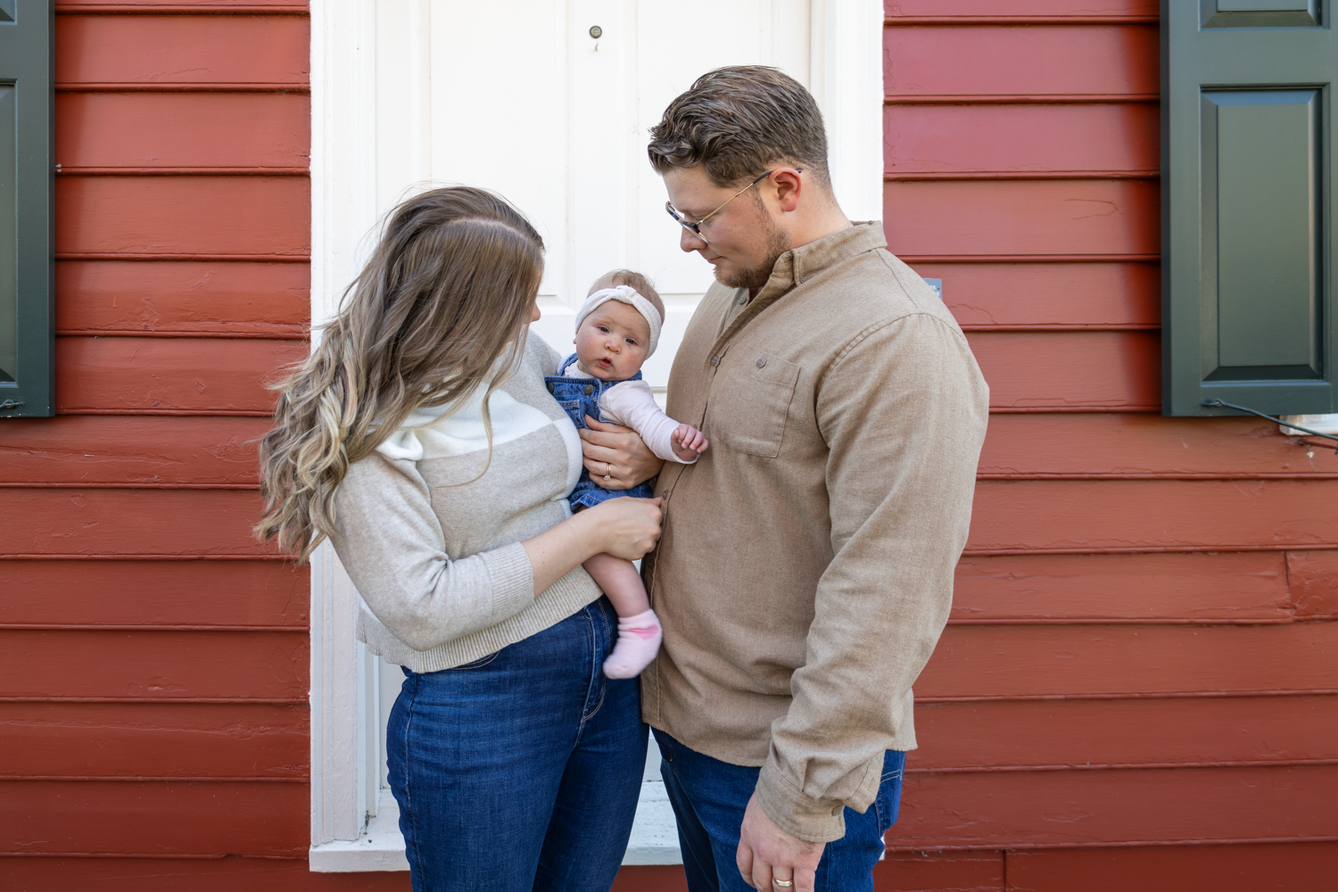 Family photos against red wooden house exterior with white trim and green shutters at Old Salem.