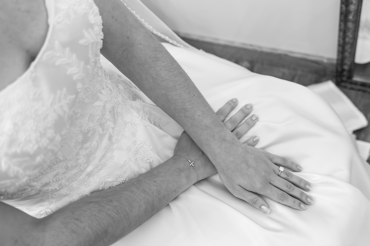 Black and white photo of a bride in a white lace dress, showcasing her elegant hand with a diamond ring and delicate bracelet.