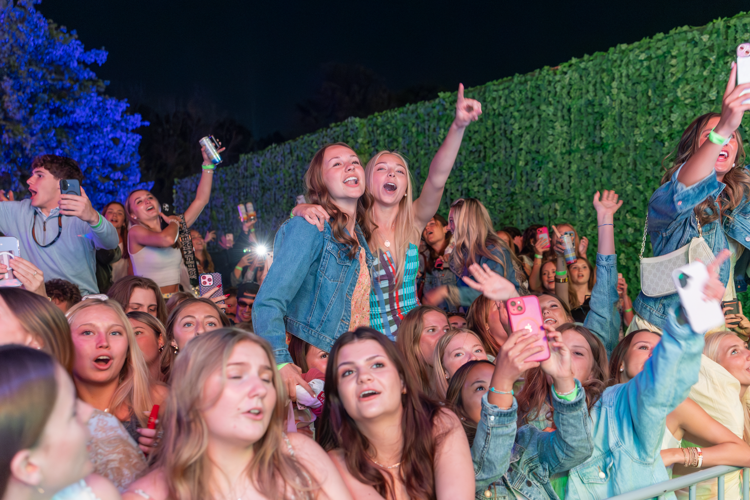 Excited crowd of young fans cheering at an outdoor concert at night, with two girls standing out in the crowd.