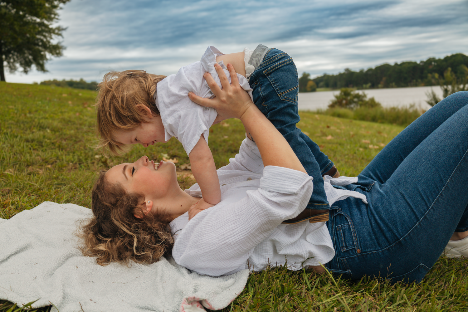 People playing and relaxing together on grassy hill overlooking water on sunny day.