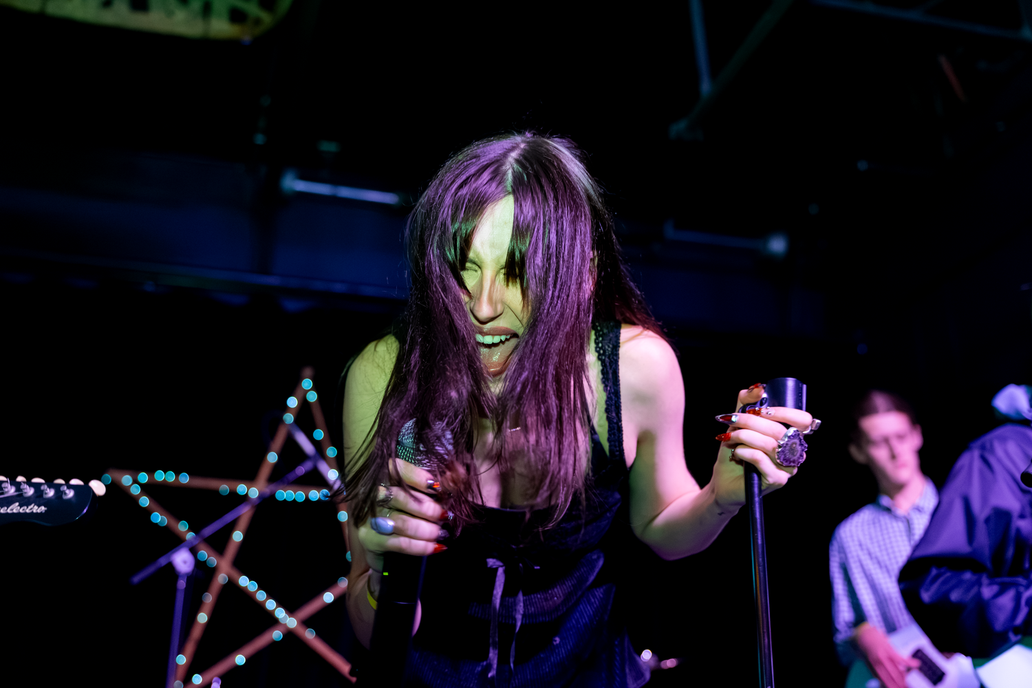 Female rock singer performing on stage under green lights, holding microphone with star decoration in background.