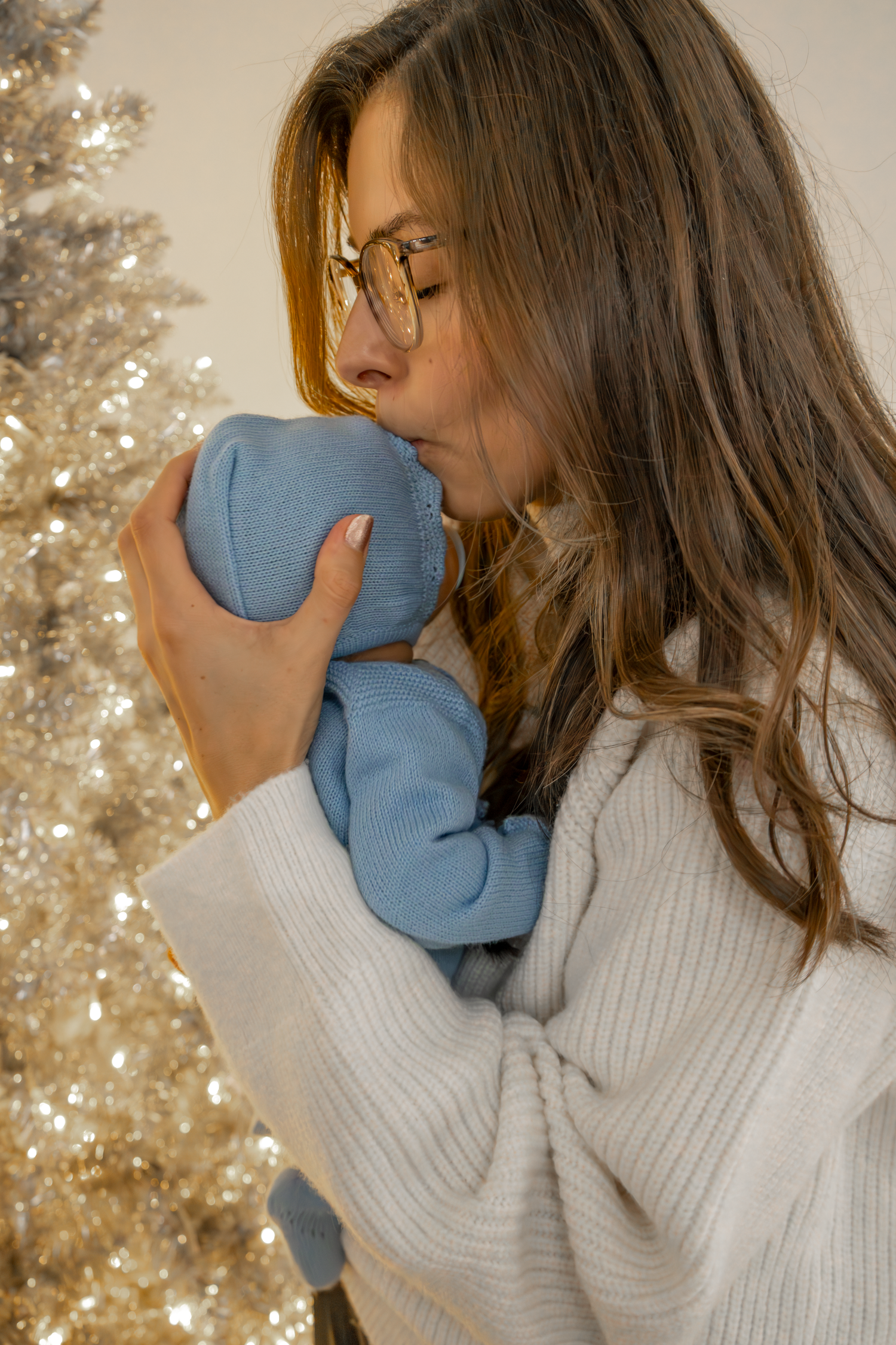 Woman in white sweater and glasses holding a blue item near a sparkly Christmas tree at The GingerBirdie Studio.