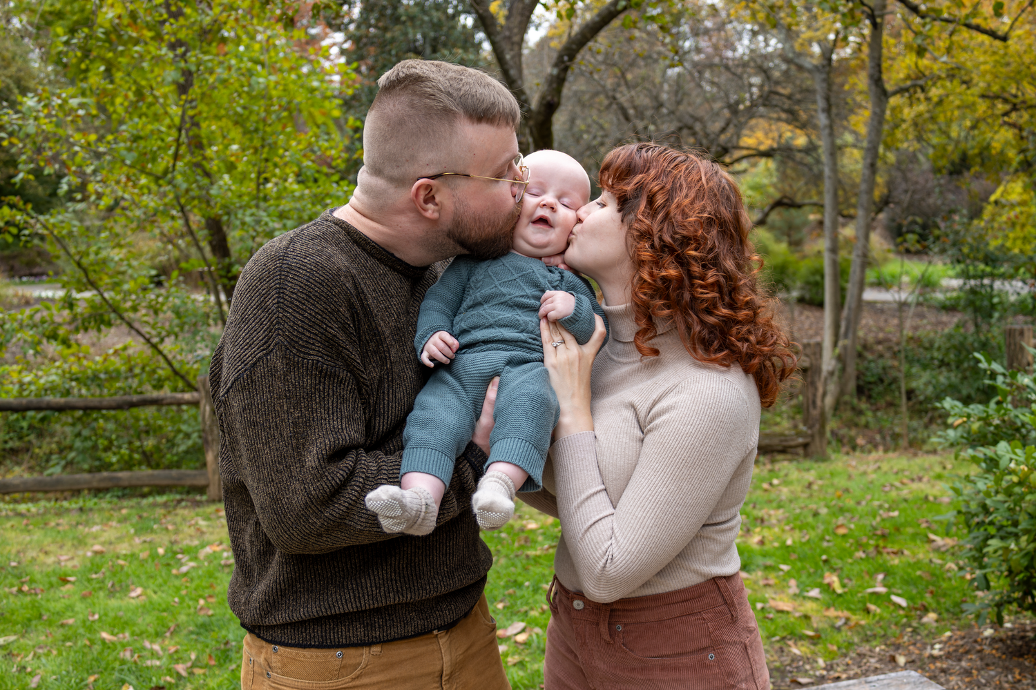 Family sharing tender moments together under trees with autumn foliage at Tanger Family Bicentennial Garden.