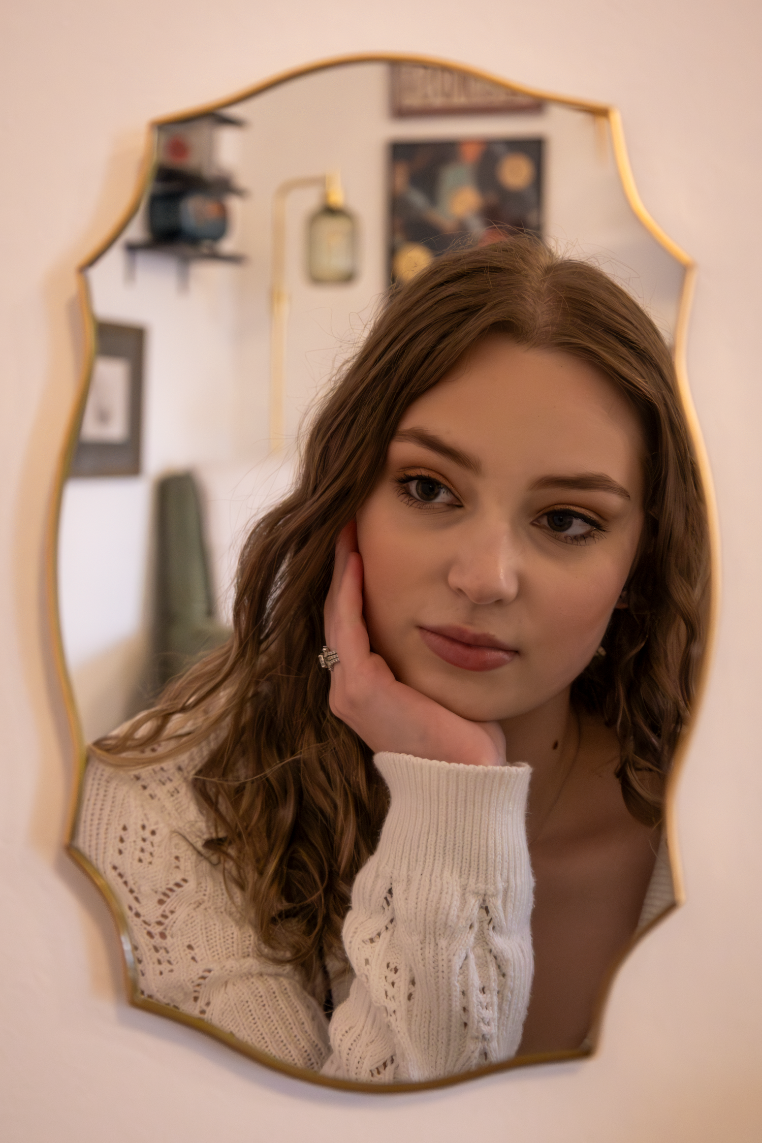 Mirror selfie showing reflection in decorative gold-framed mirror against plain wall.