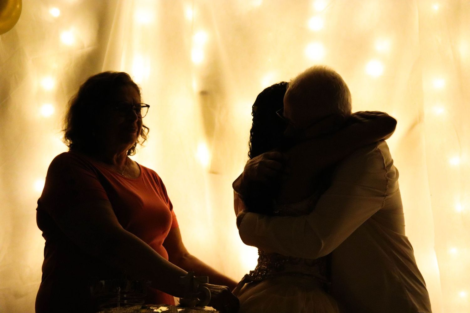 fotografia de silhueta em festa de aniversário de 15 anos com a debutante abraçando os avós.