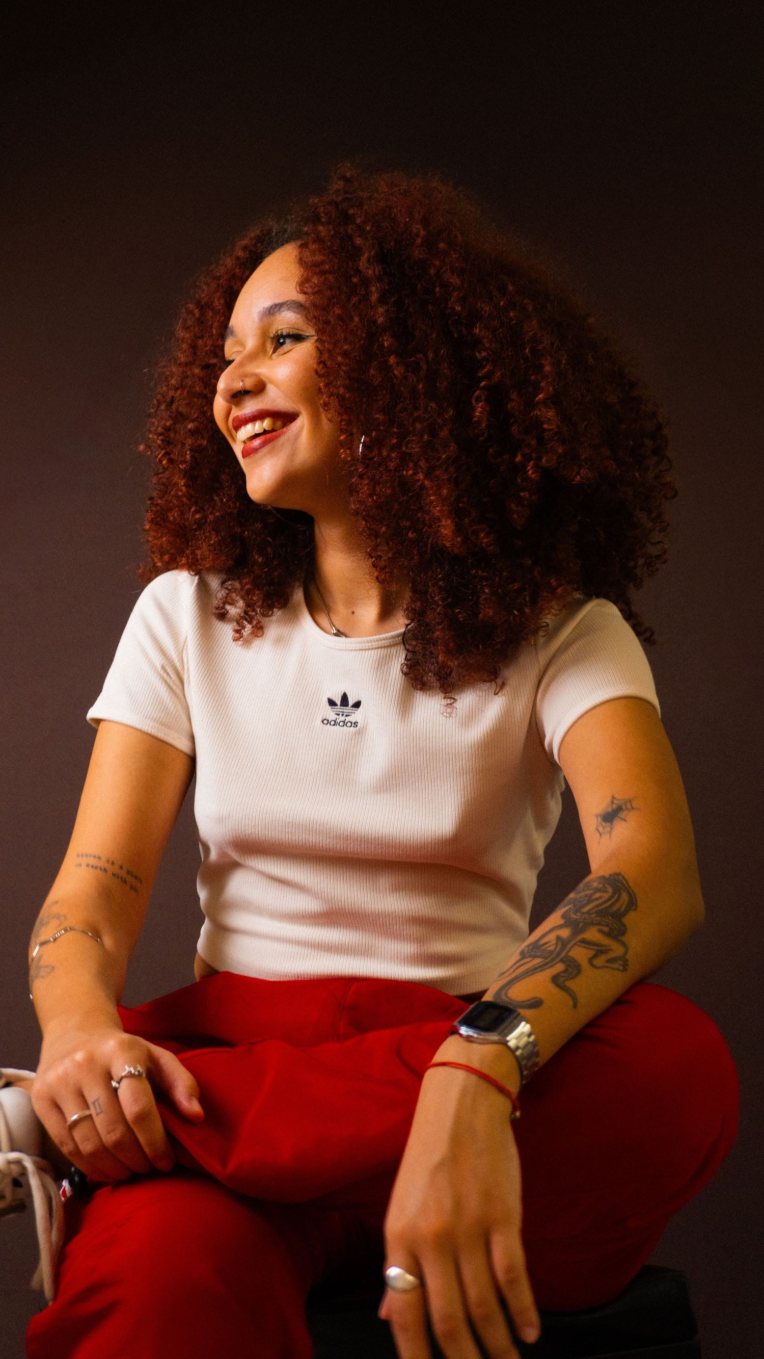 ensaio feminino em estúdio. a mulher está sentada olhando para o lado esquerdo e sorrindo, com as pernas cruzadas.