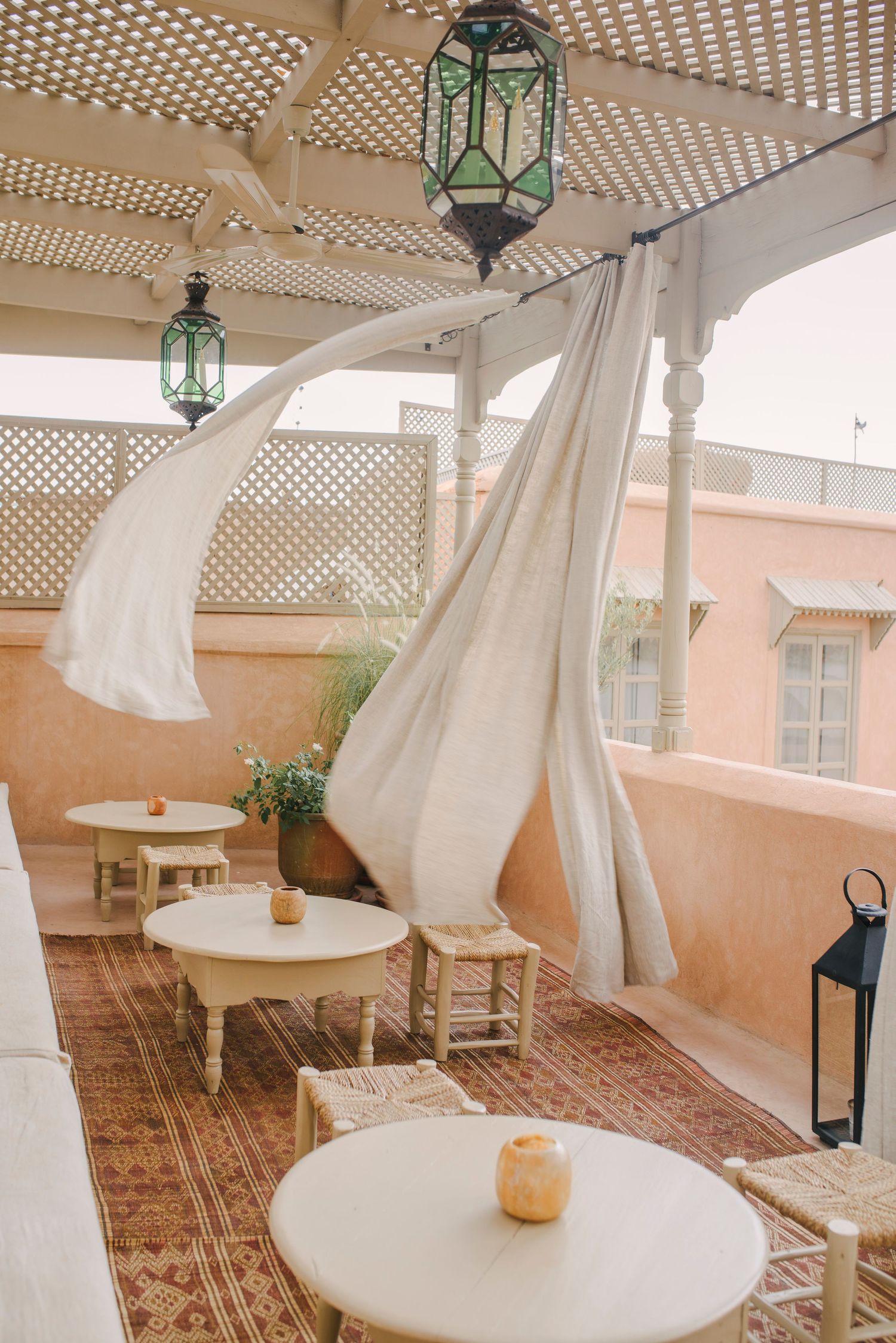 Outdoor terrace with white lattice pergola, flowing curtains, and Moroccan lanterns.