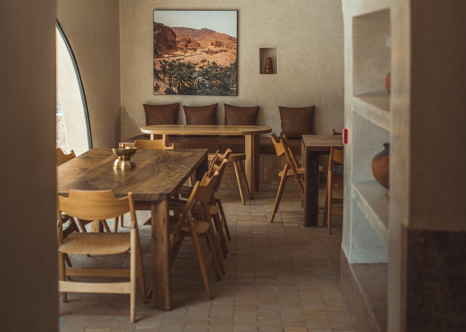 Interior of a cozy restaurant dining room with wooden tables, chairs and landscape artwork on tan walls.