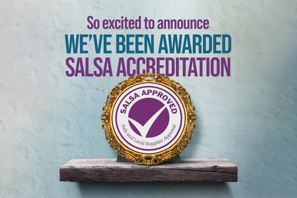 Circular gold and purple accreditation badge announcing salsa certification award displayed on wooden shelf against blue wall.
