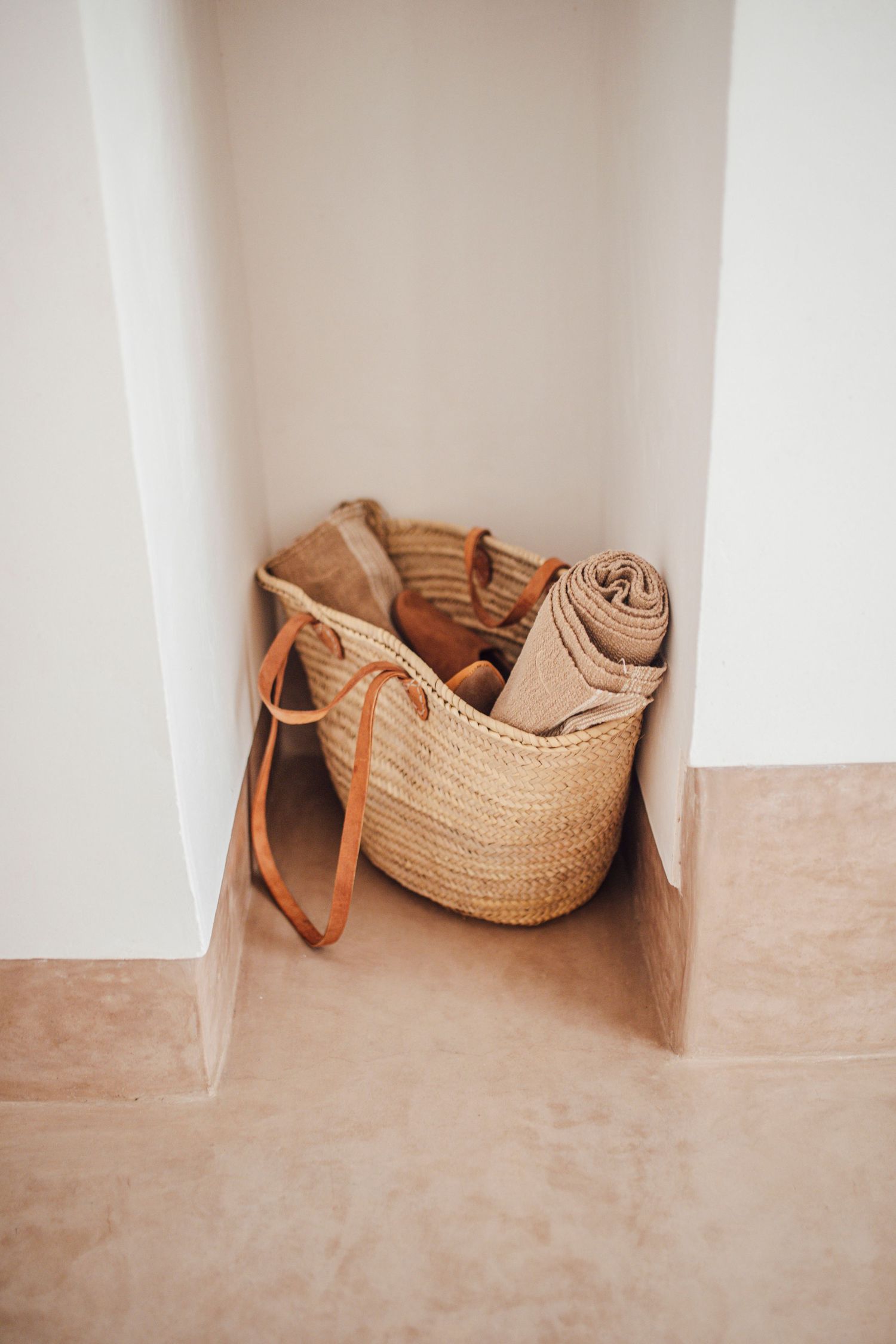 Woven straw basket with beige textiles stored in white wall niche.