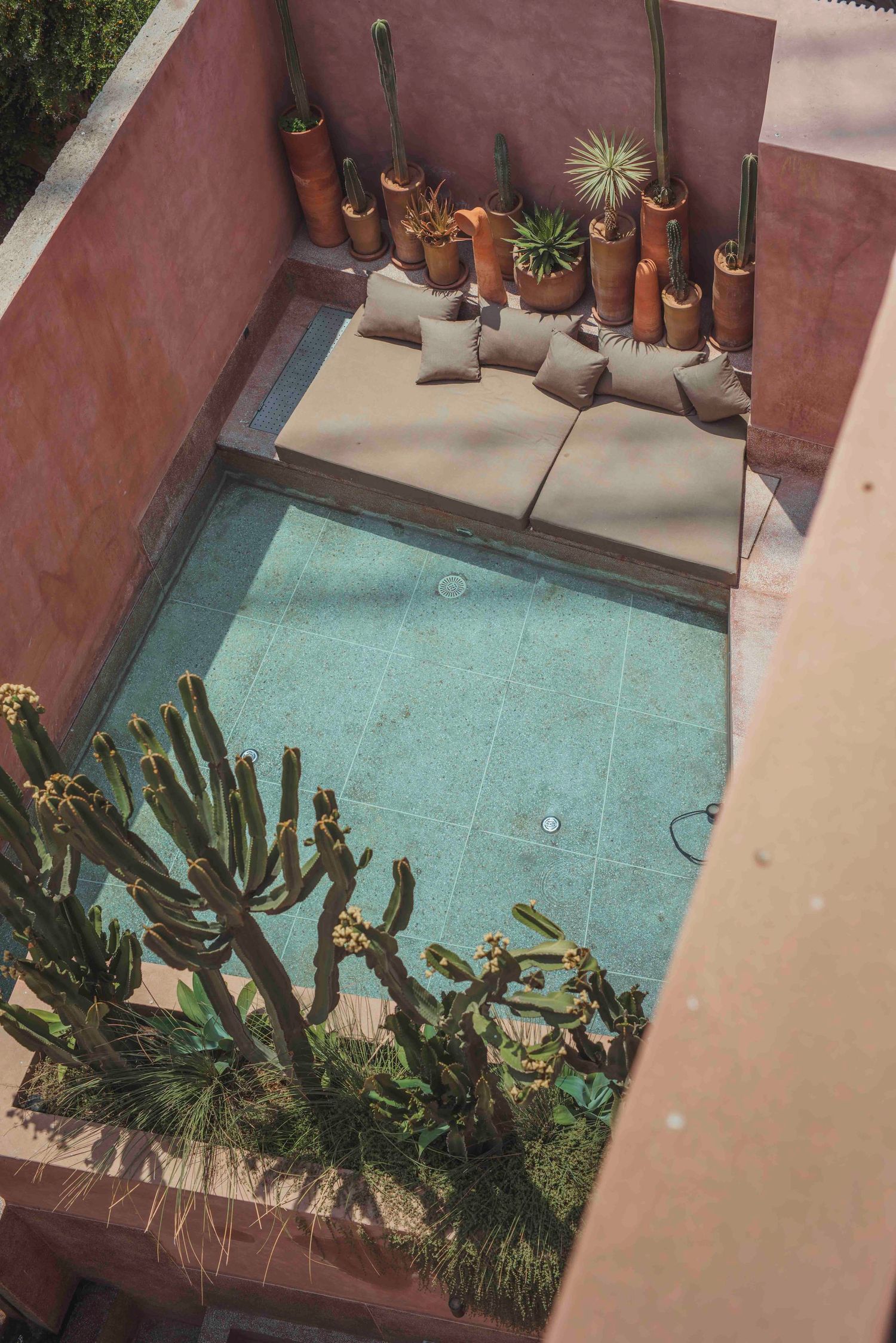 Aerial view of a turquoise pool surrounded by terracotta walls and potted cacti in a modern courtyard setting.