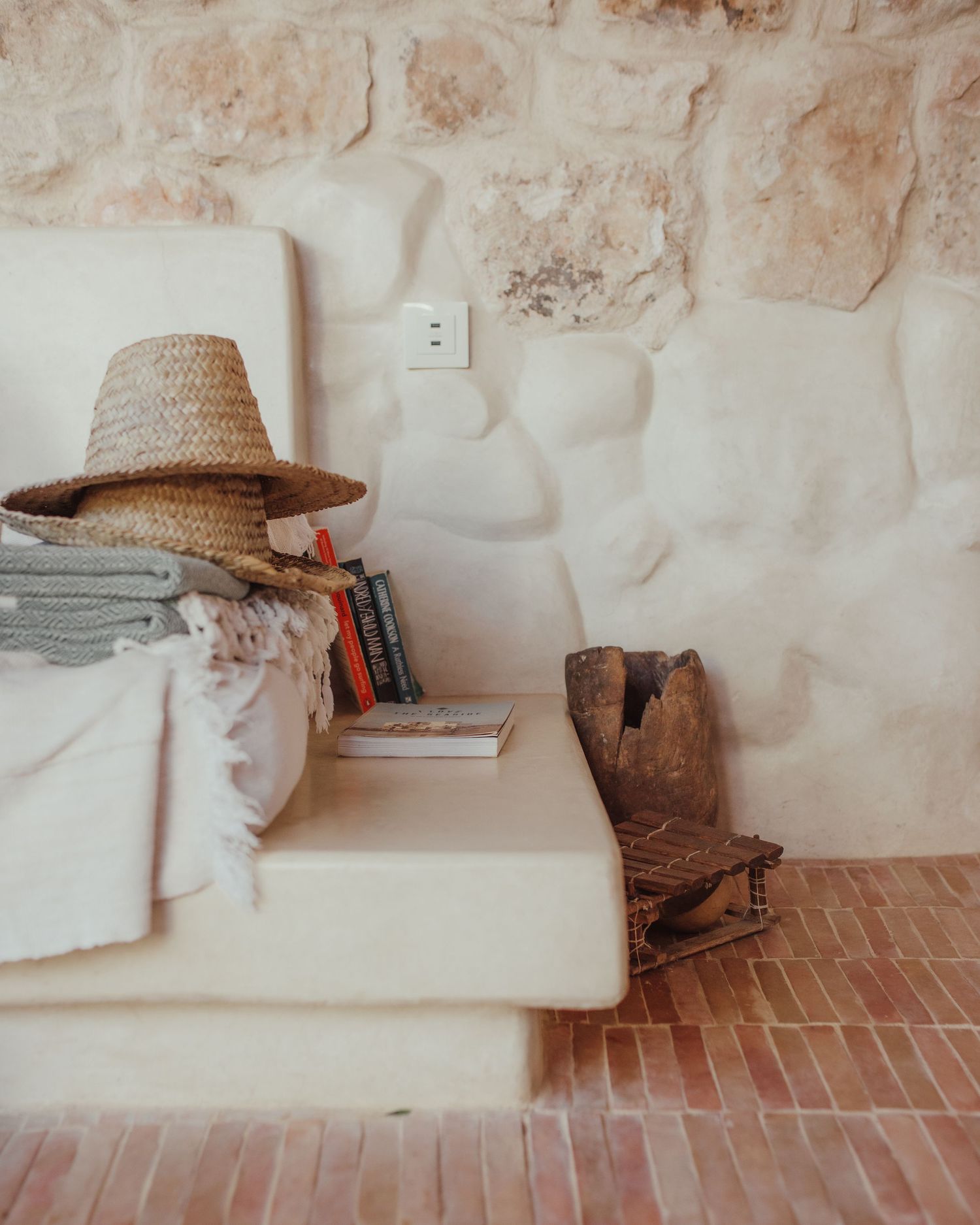 Cozy reading nook with straw hat and books against stone wall interior.