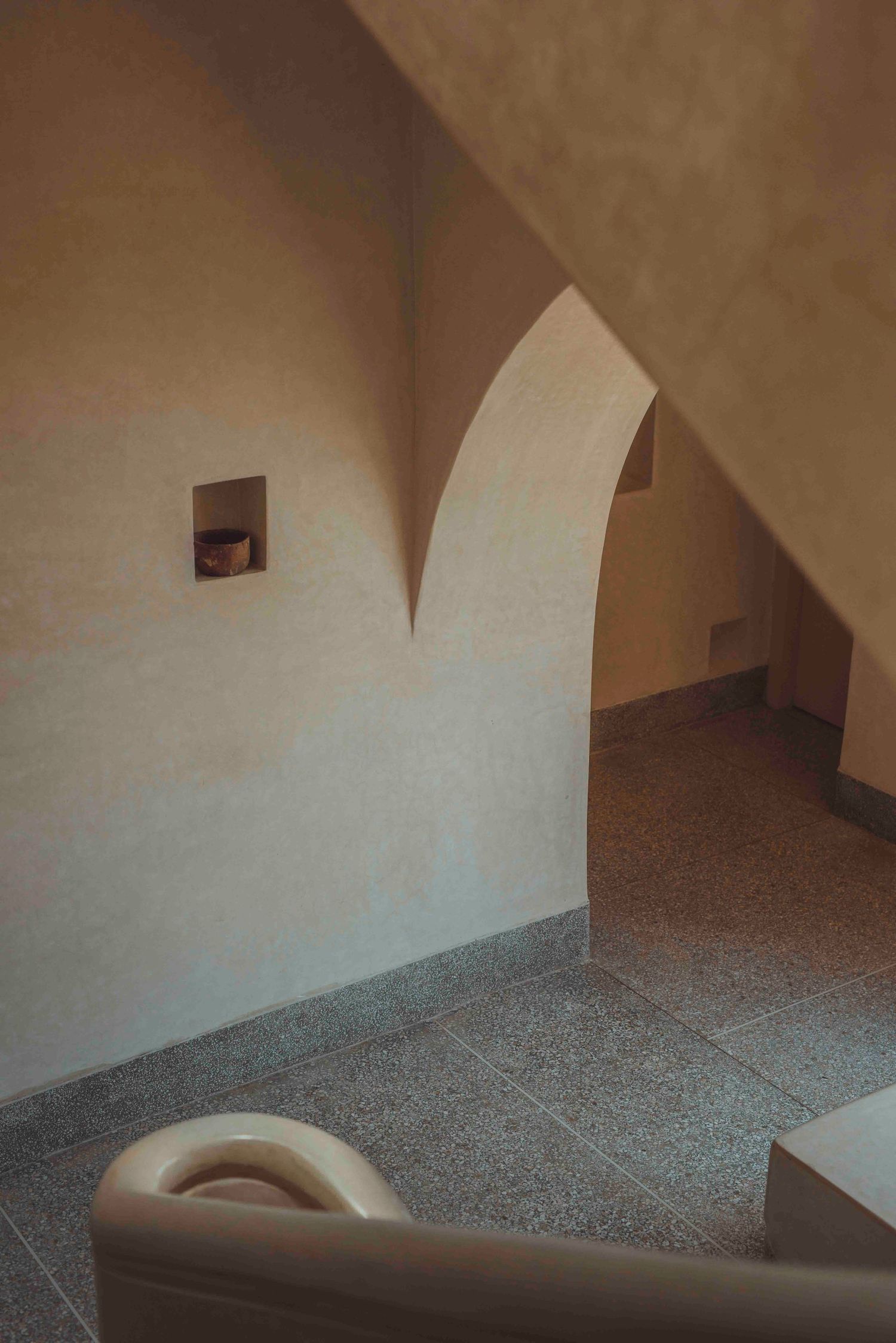 Minimalist interior architecture featuring curved archway and textured walls.